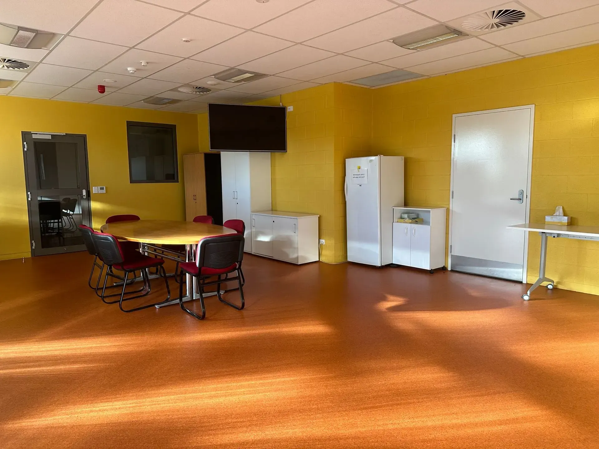 Empty room with orange floor, yellow walls, table and chairs, appliances, and a TV.