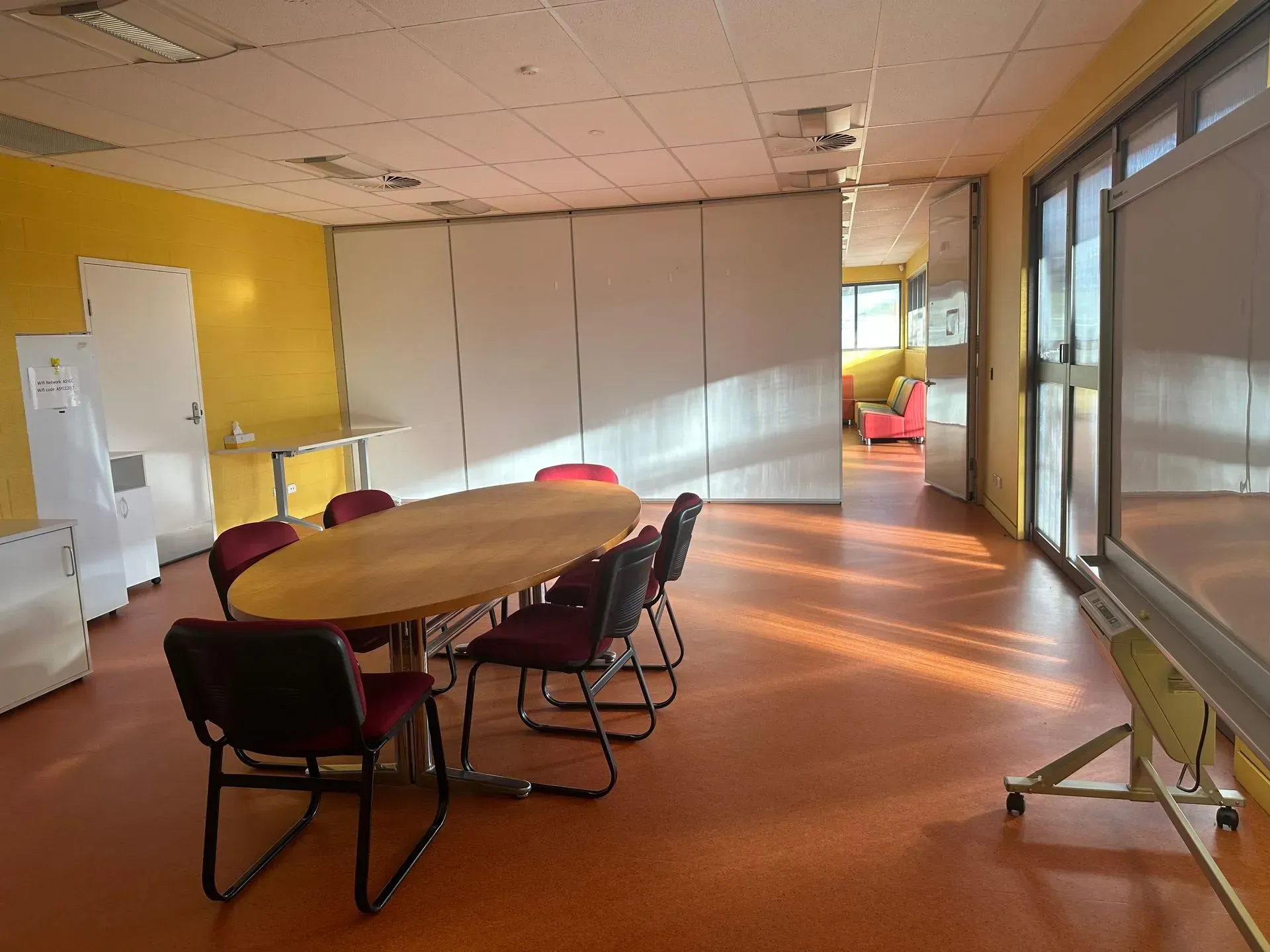 Conference room with oval table, chairs, whiteboard, and sliding glass doors. Bright orange floor and yellow wall.