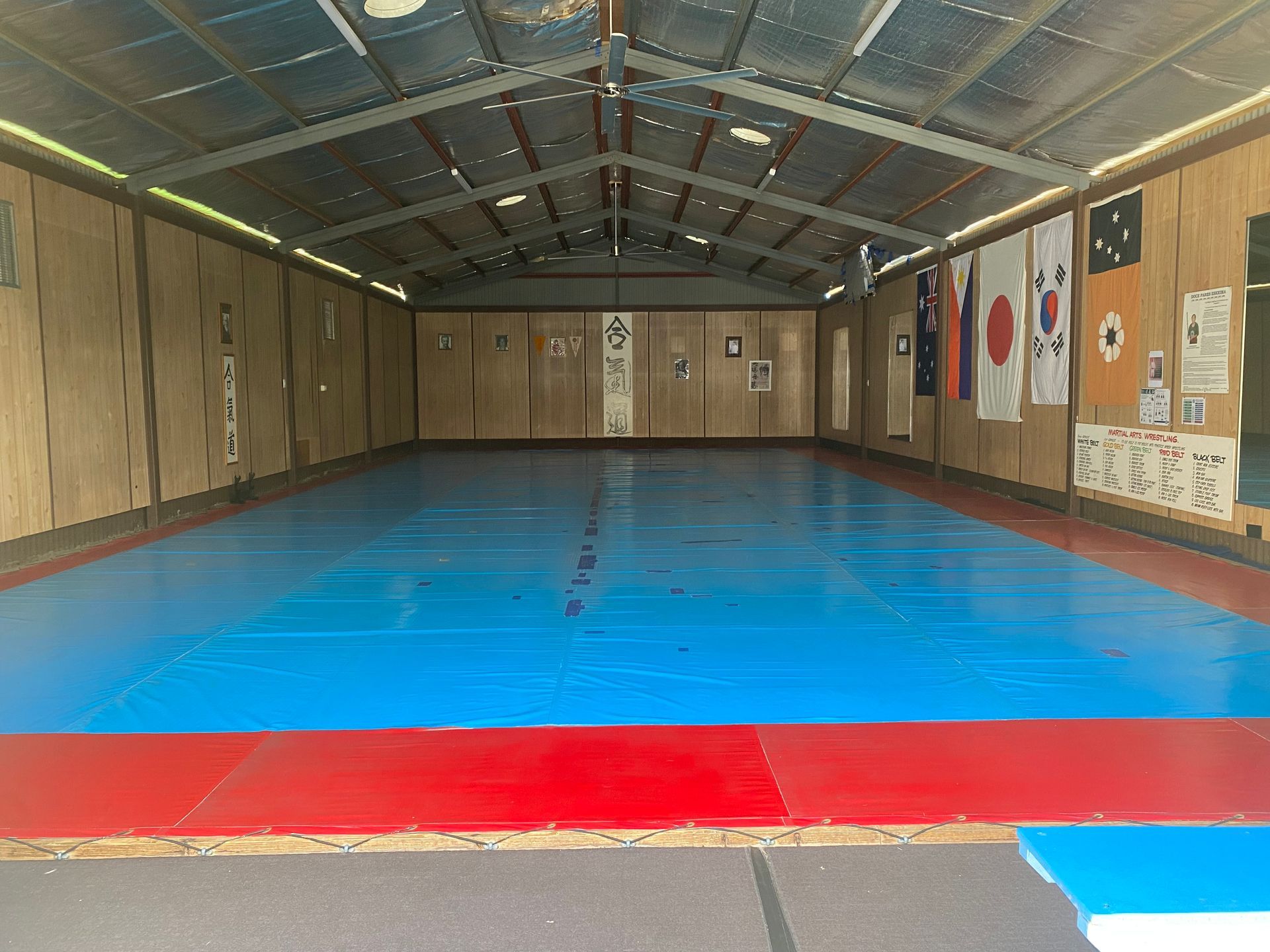 Blue and red mat in a martial arts dojo with flags and wooden walls.