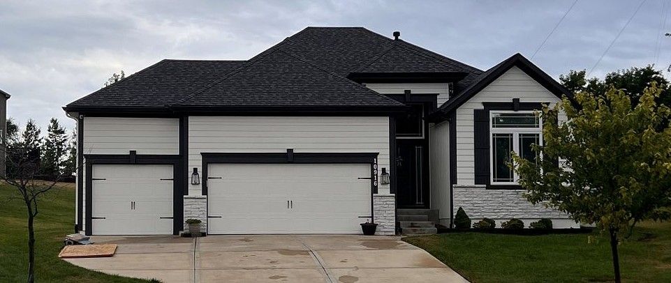A large white house with a black roof and two garage doors.