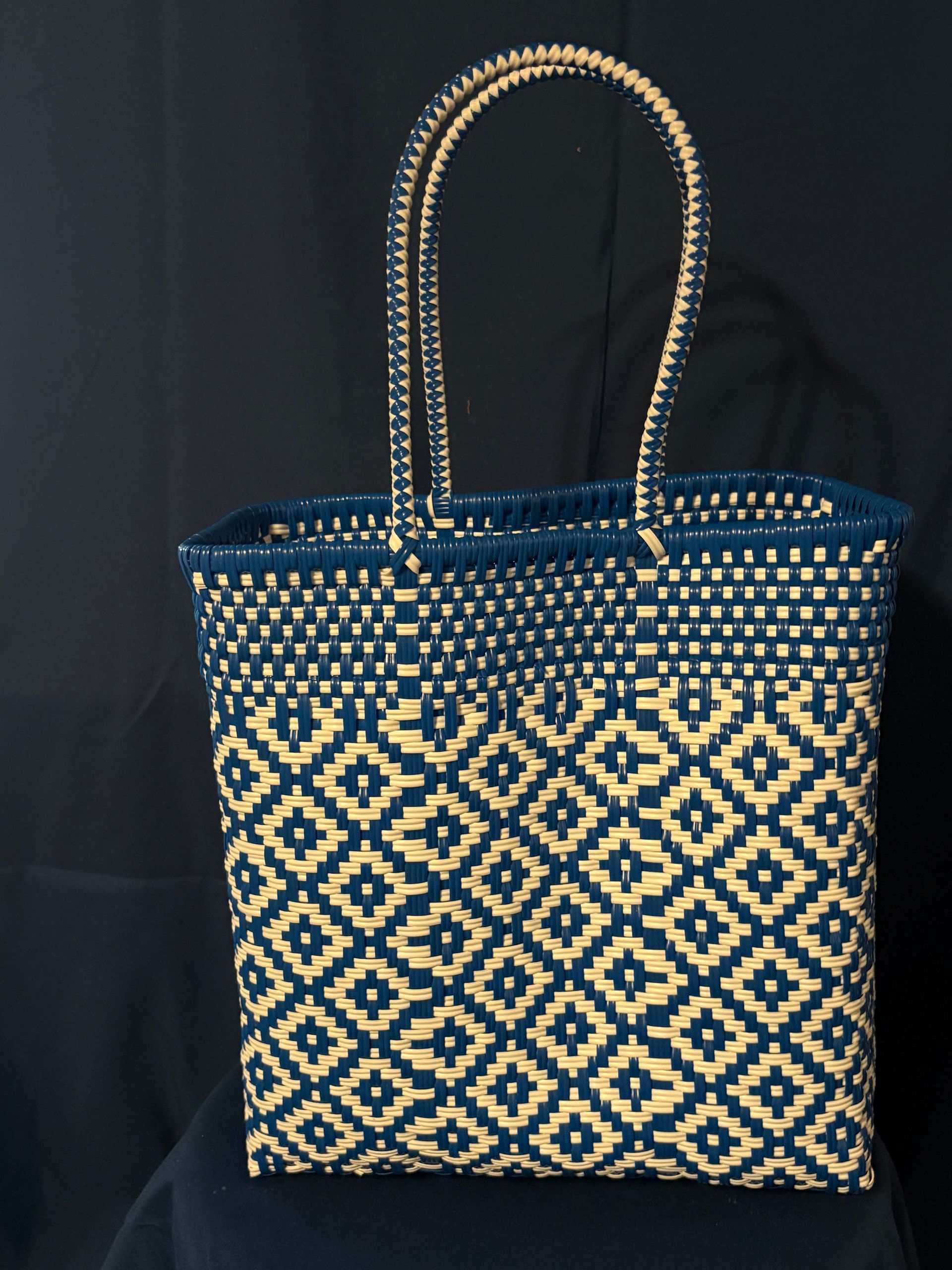 Red woven tote bag with yellow pattern and handles on a black background