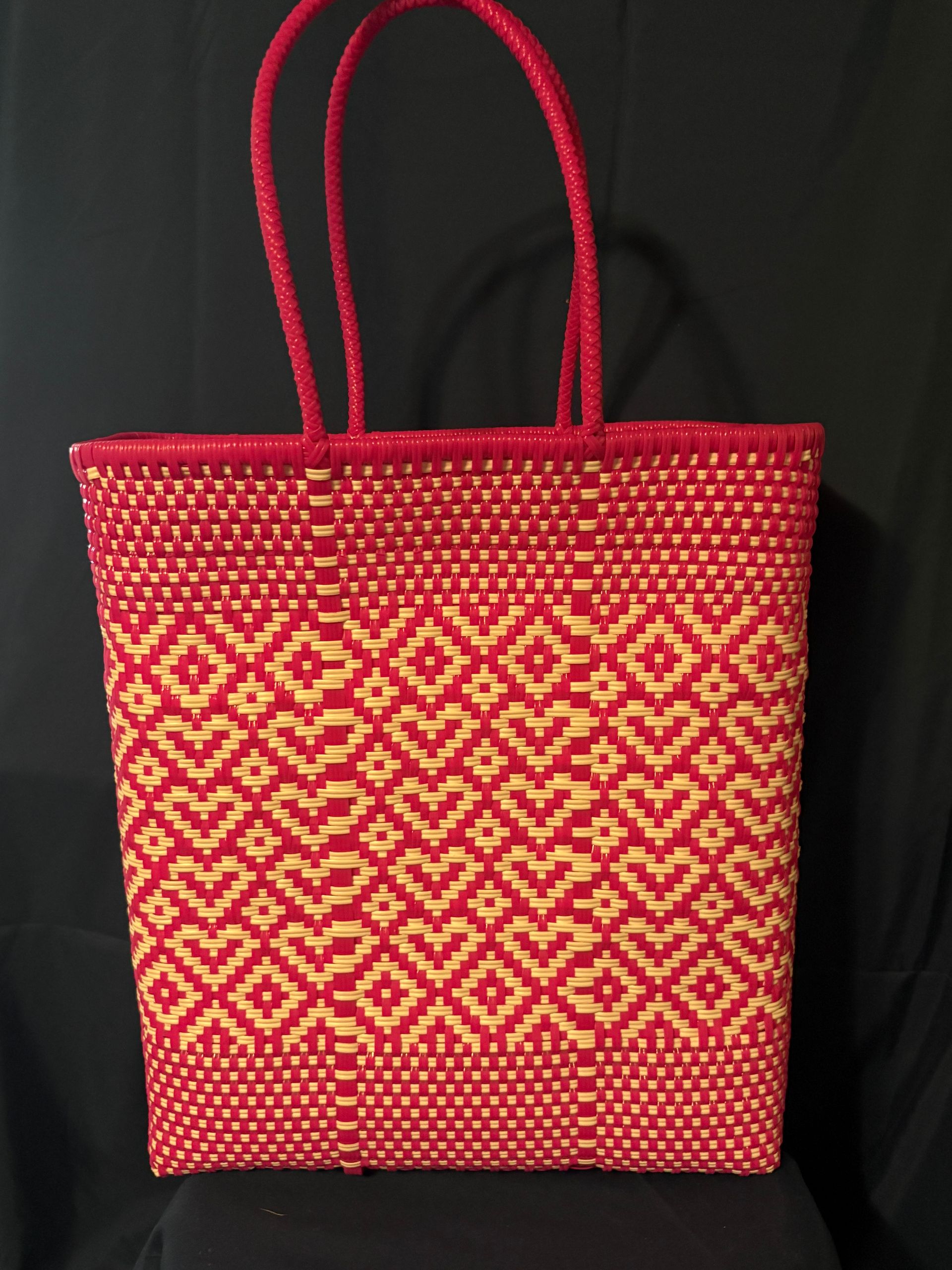 Red woven tote bag with yellow pattern and handles on a black background