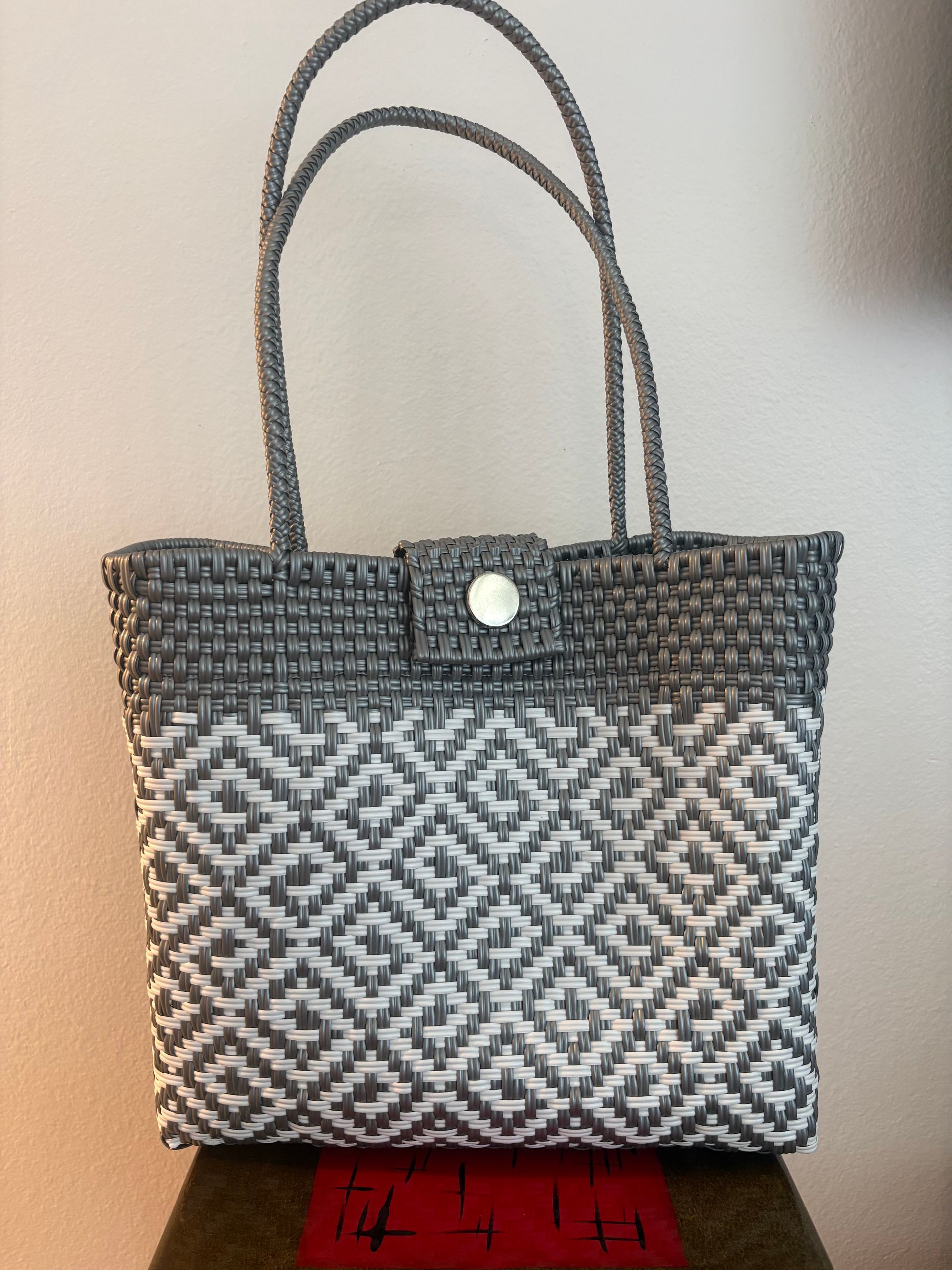 Gray woven handbag with double handles and a button closure on a red surface.