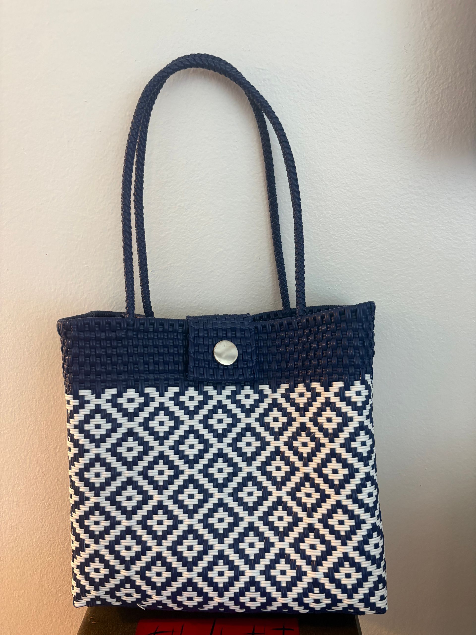 Blue-and-white patterned tote bag with long handles hanging against a light wall