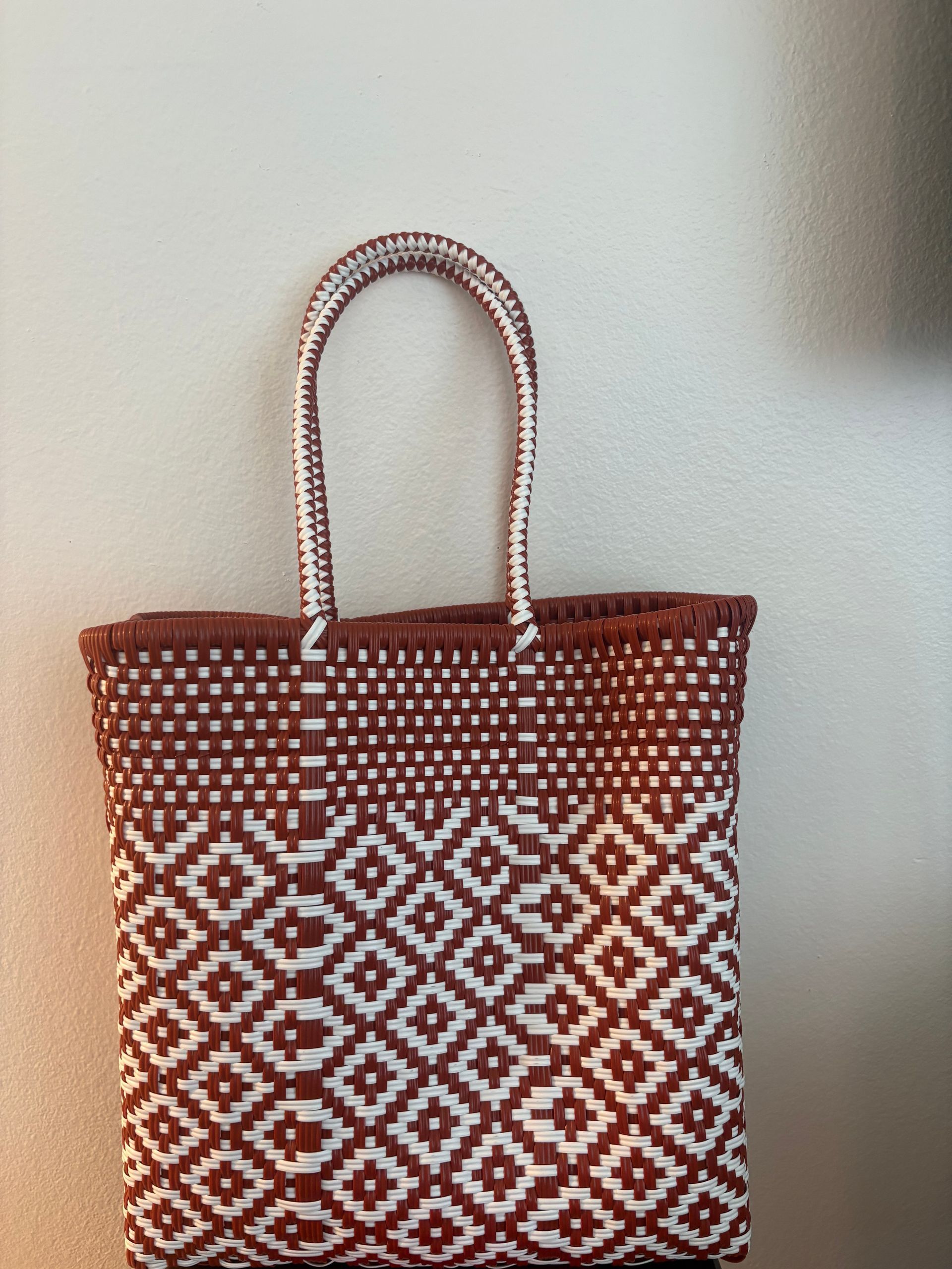 Red and white patterned woven tote bag hanging on a light wall