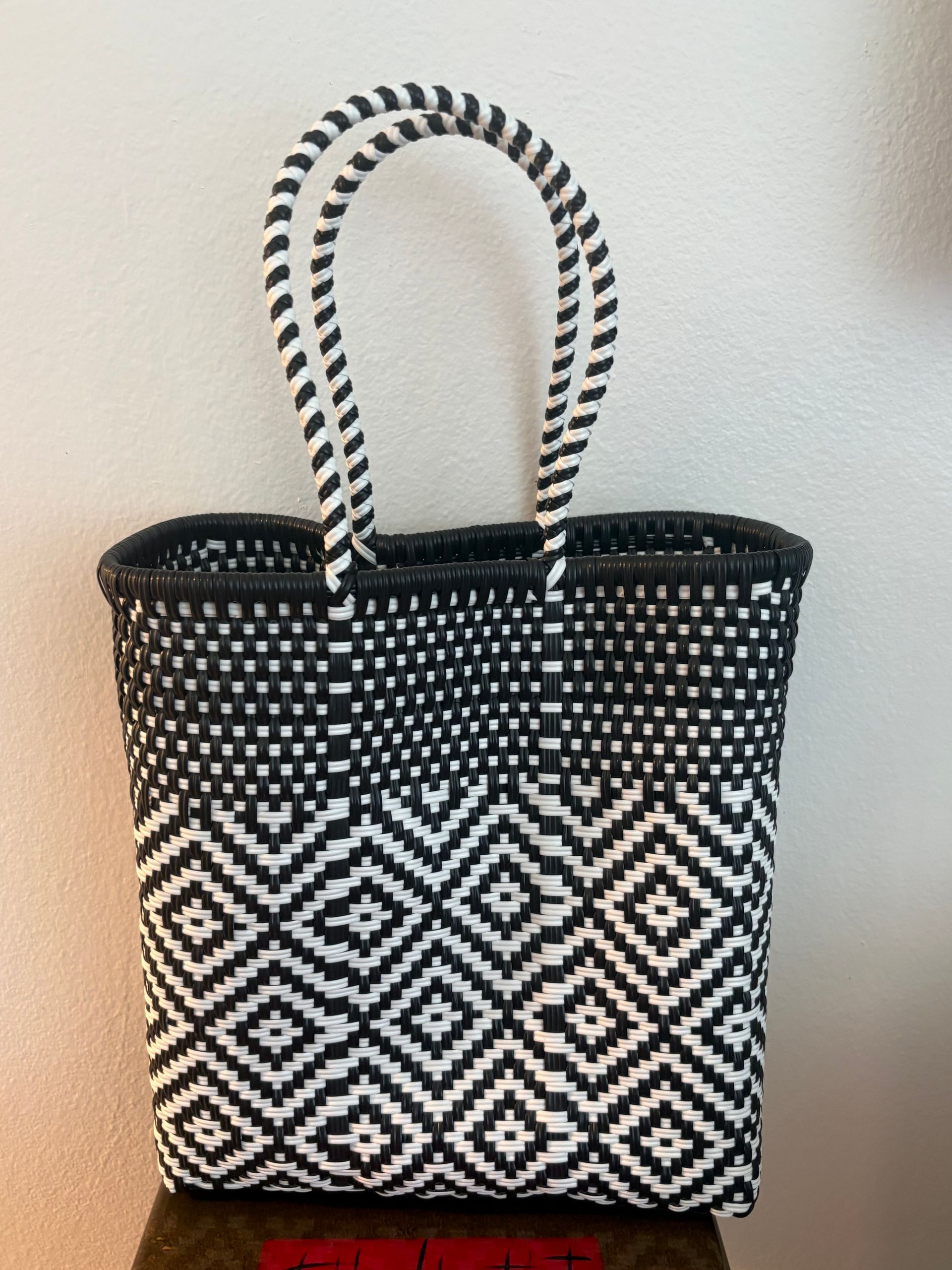Black-and-white woven tote bag with geometric pattern and striped handles against a plain wall