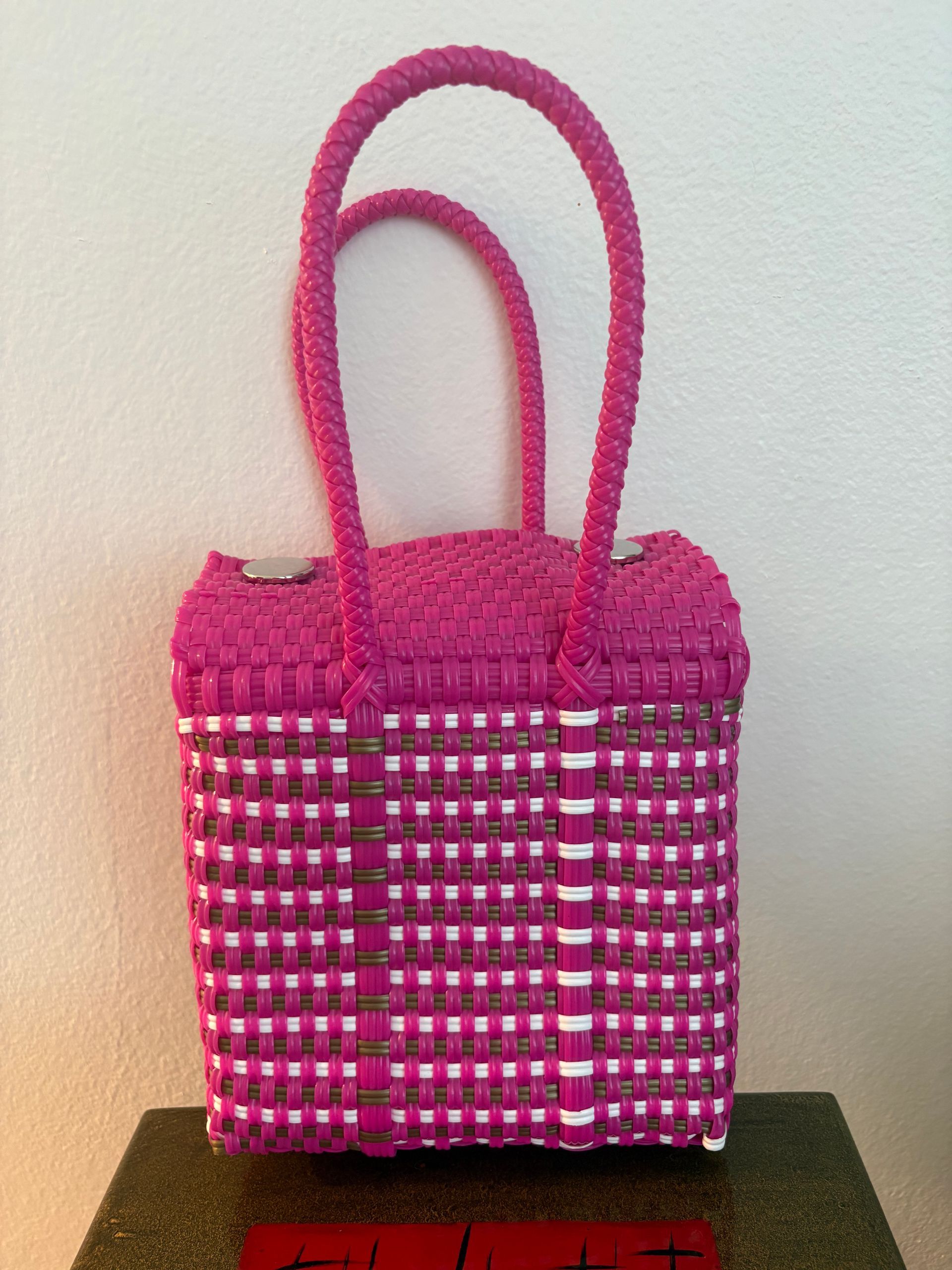 Pink woven tote bag with tall handles, standing on a dark surface against a plain wall