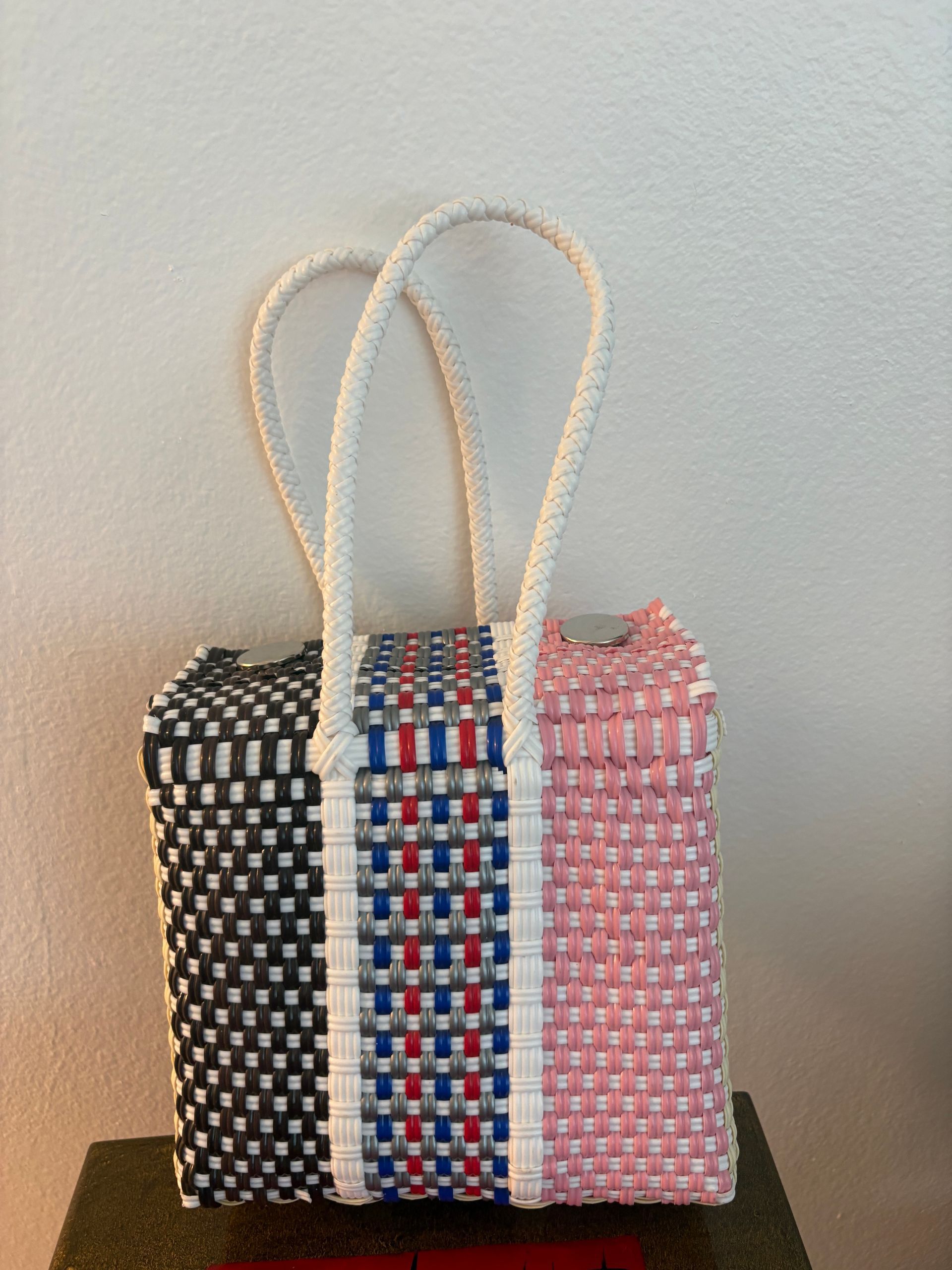 Three woven tote bags in black, blue-red-white, and pink, with rope handles, on a dark surface.