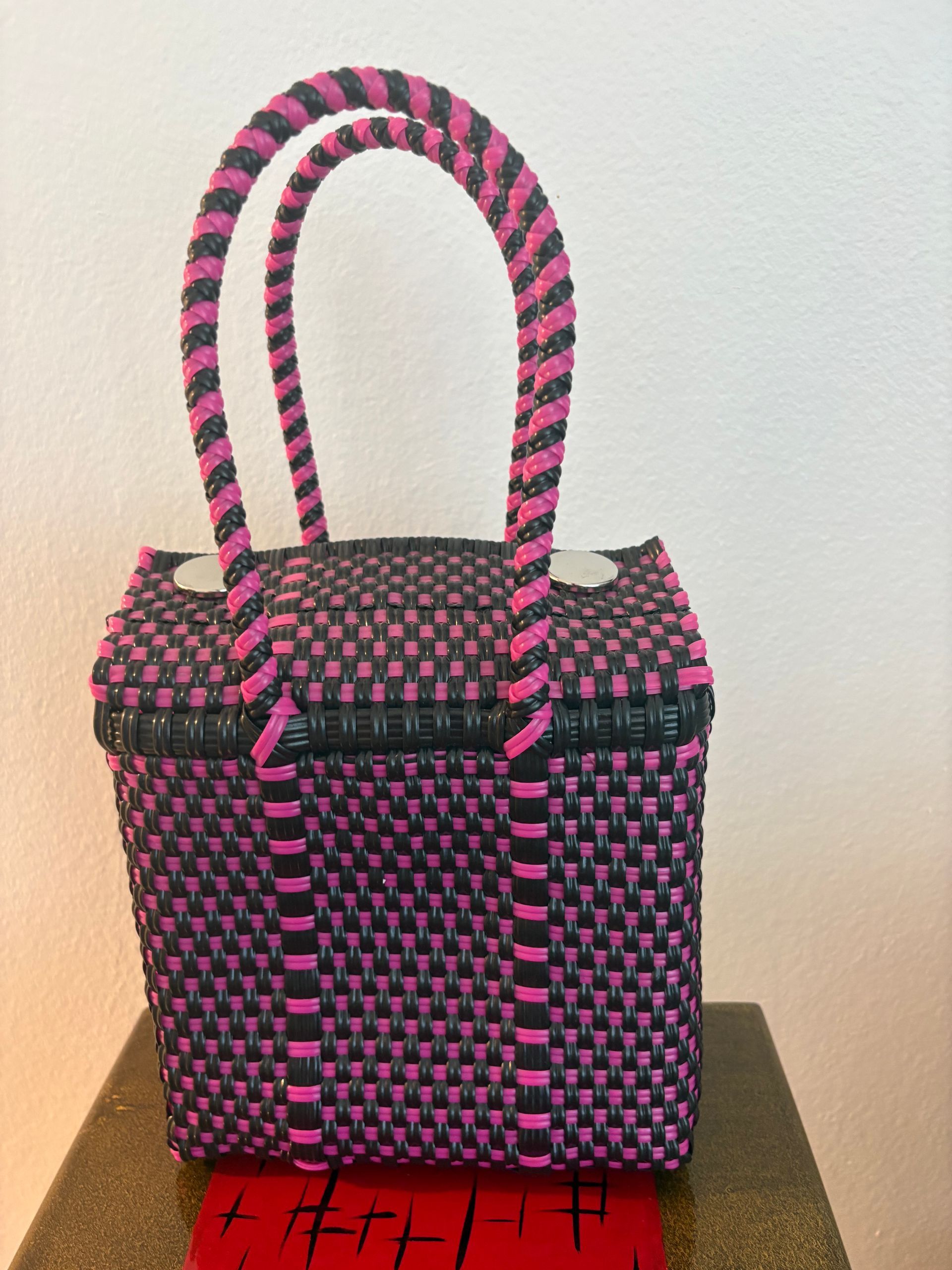 Pink and black woven handbag with long handles on a table against a plain wall
