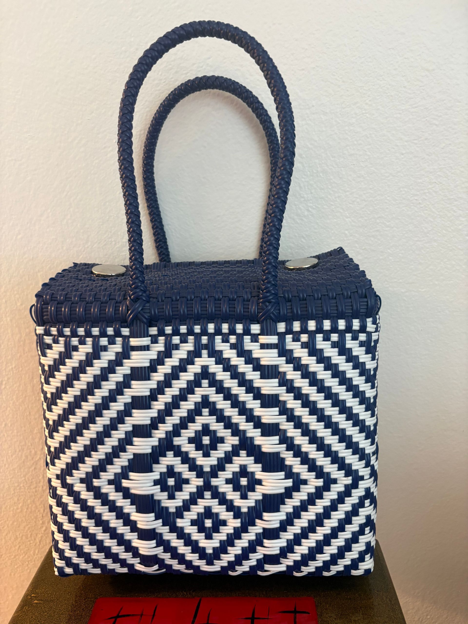 Blue-and-white woven tote bag with geometric pattern and double handles against a light wall.