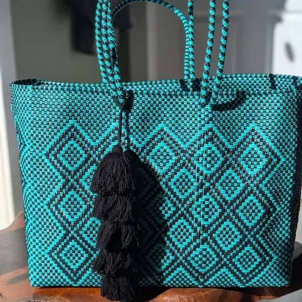 Turquoise woven tote bag with black geometric pattern and black tassel on a table