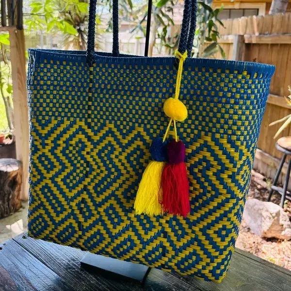 Blue-and-yellow woven tote bag with zigzag pattern and tassel hanging outdoors
