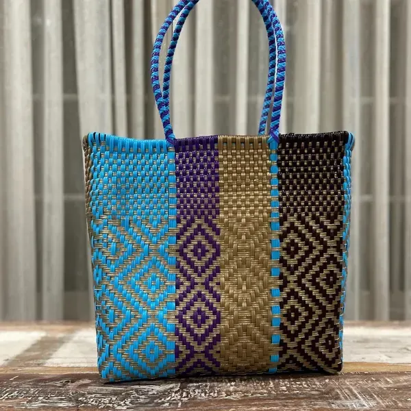 Colorful woven tote bag with blue handles on a tabletop in front of curtains