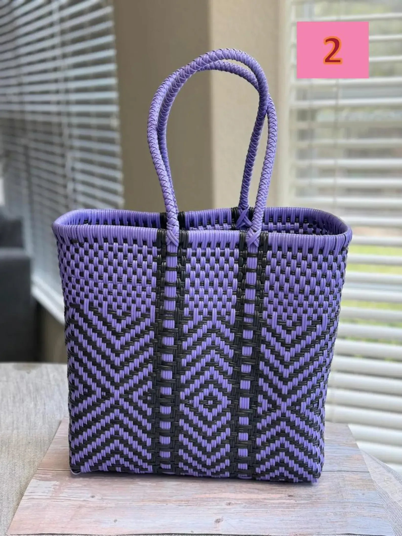 Purple woven tote bag with black zigzag pattern and loop handles on a wooden table, marked with a pink “2” tag