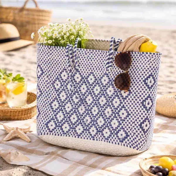 Blue patterned woven tote on a picnic table, filled with flowers, bread, sunglasses, and a lemon.