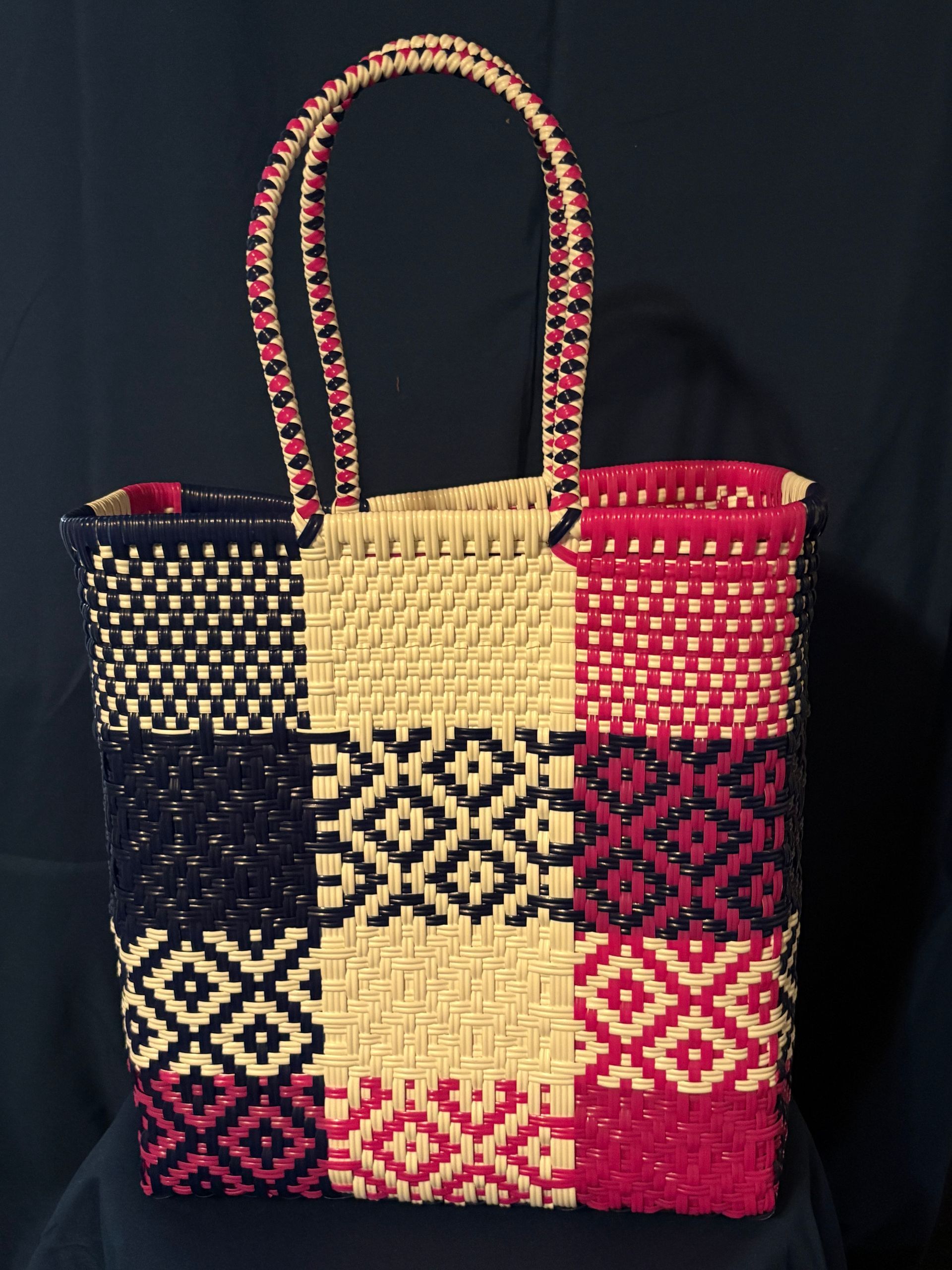Colorful woven tote bag with braided handles and geometric patterns in black, cream, pink, and red