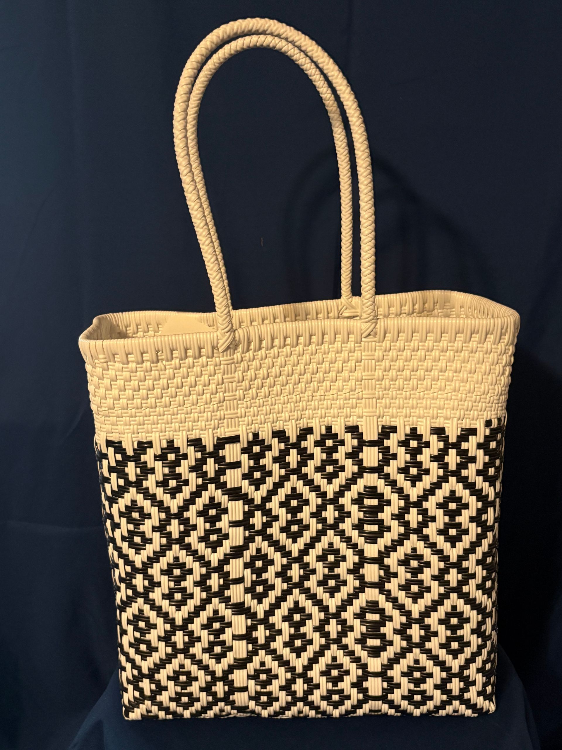 Woven straw tote bag with black geometric pattern and tall loop handles on a dark background