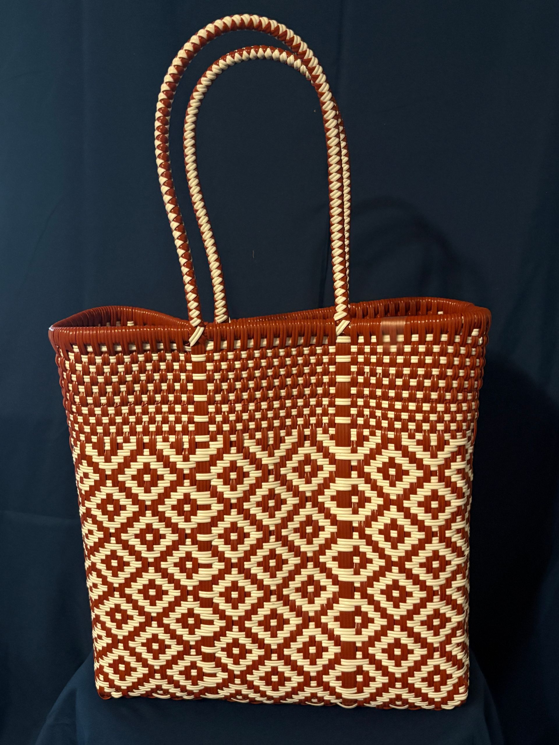 Woven brown tote bag with white geometric pattern and looped handles on a dark background