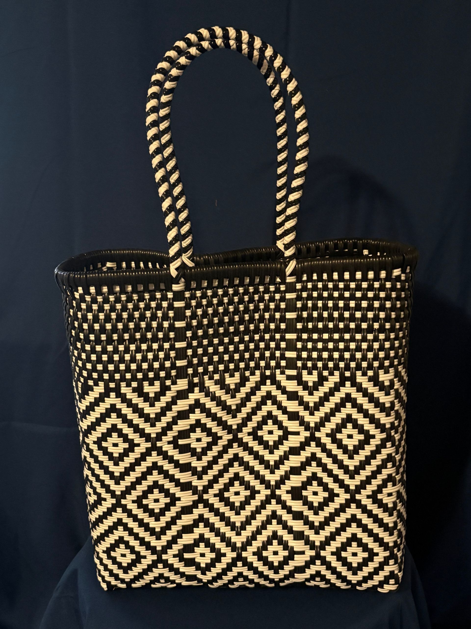 Black-and-white patterned woven tote bag with braided handles on a dark blue background
