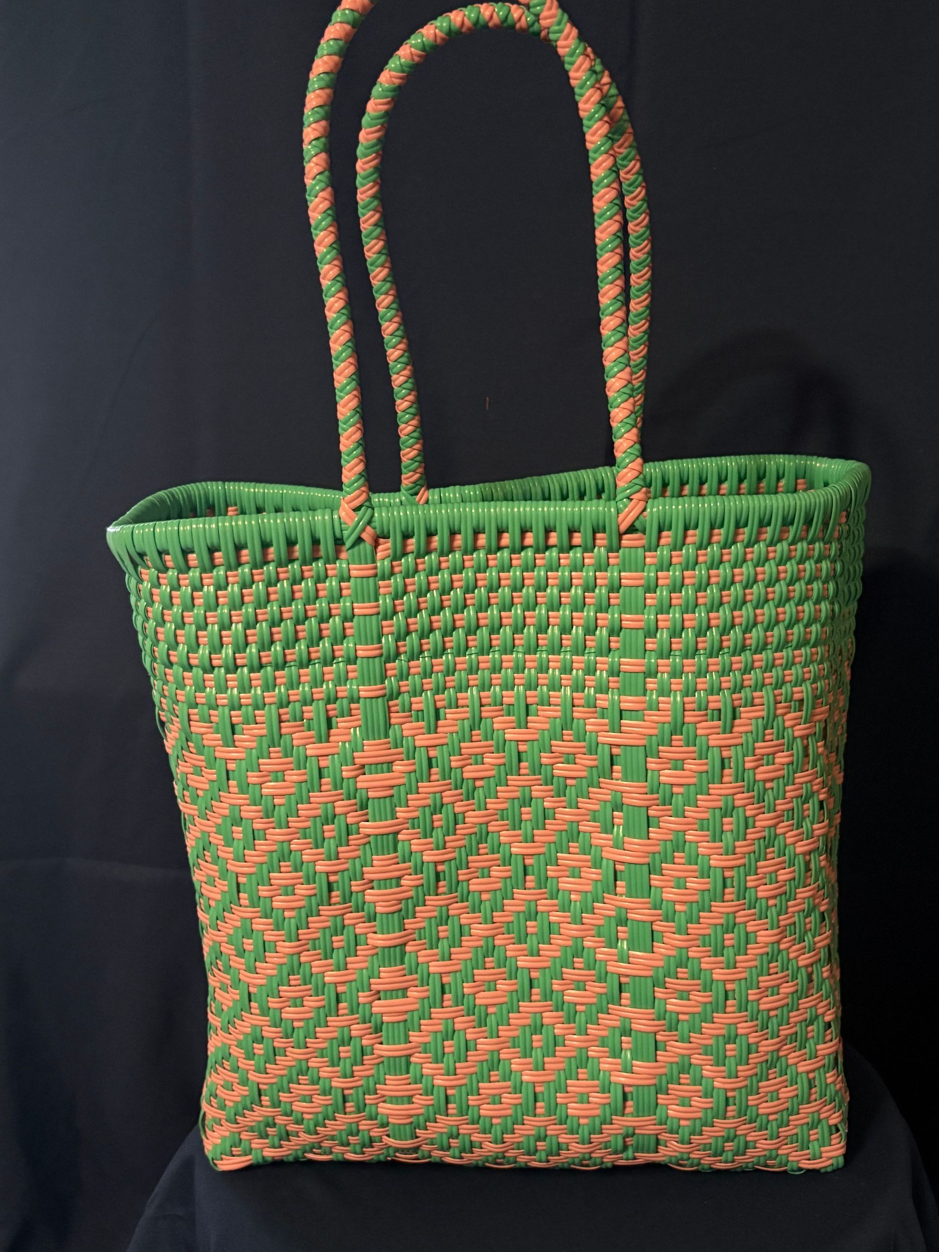 Green-and-orange woven tote bag with long braided handles on a dark background