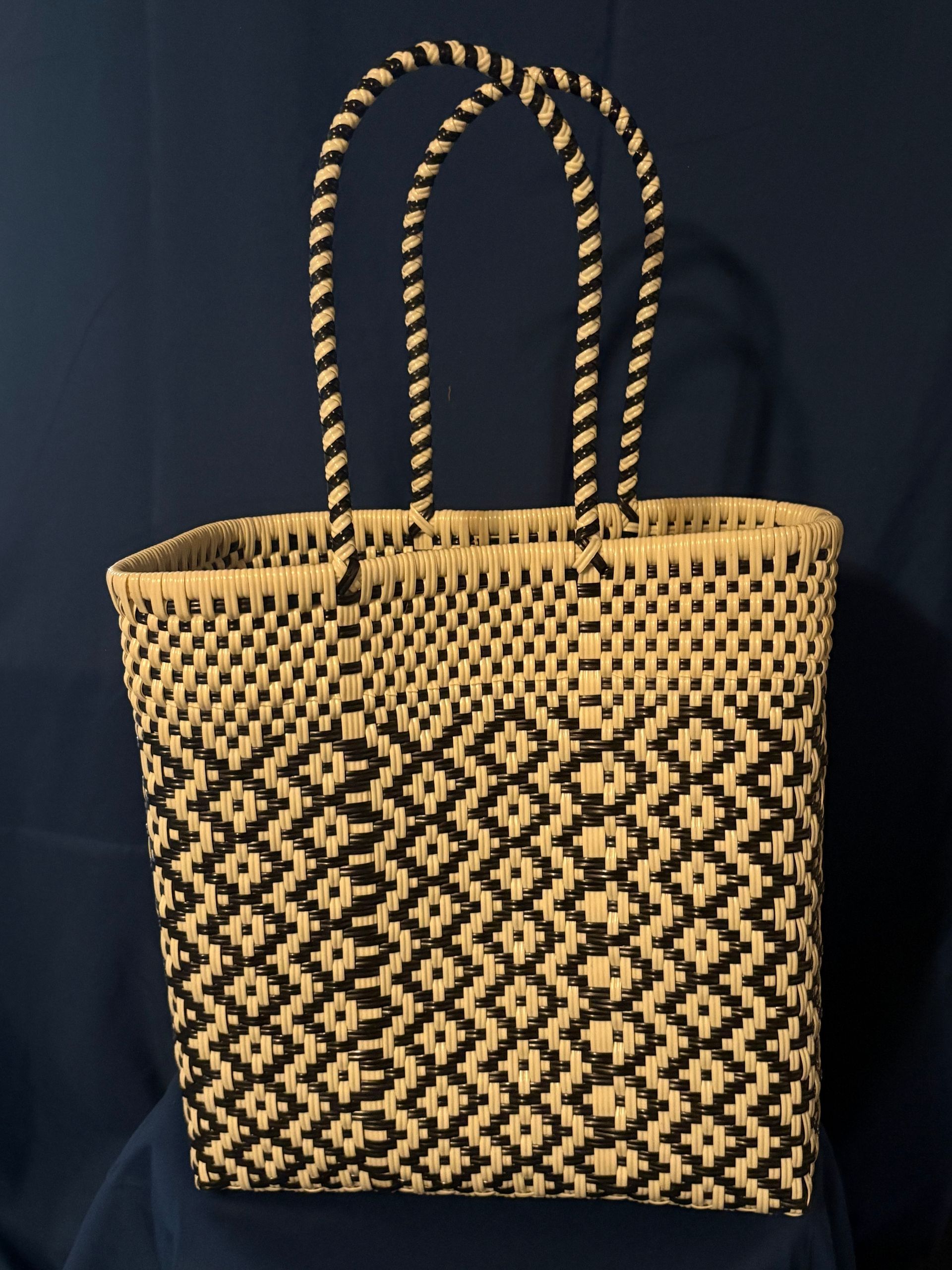 Woven straw tote bag with black geometric pattern and tall braided handles on a dark background