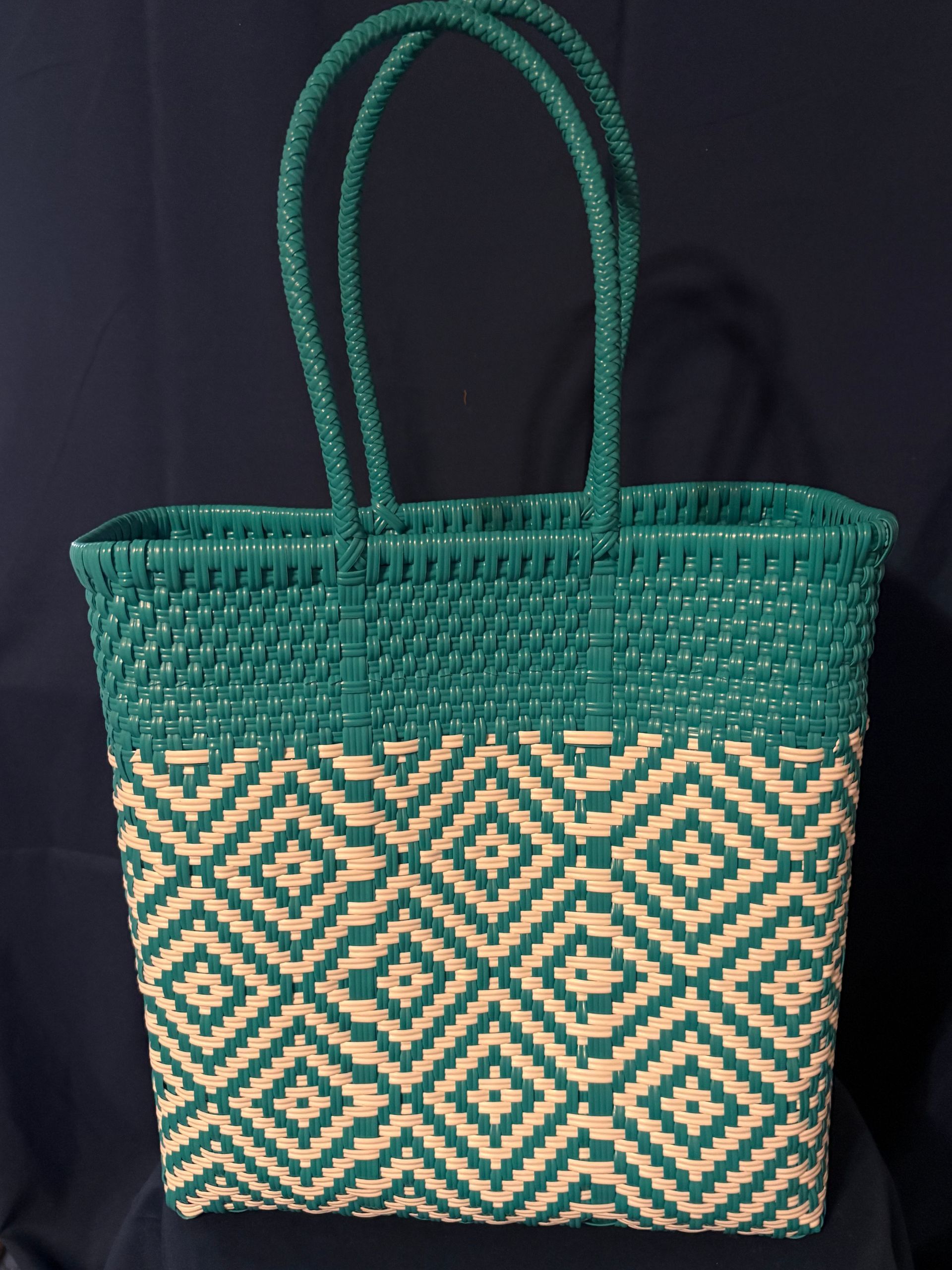 Green woven tote bag with tan geometric pattern and double handles against a dark background