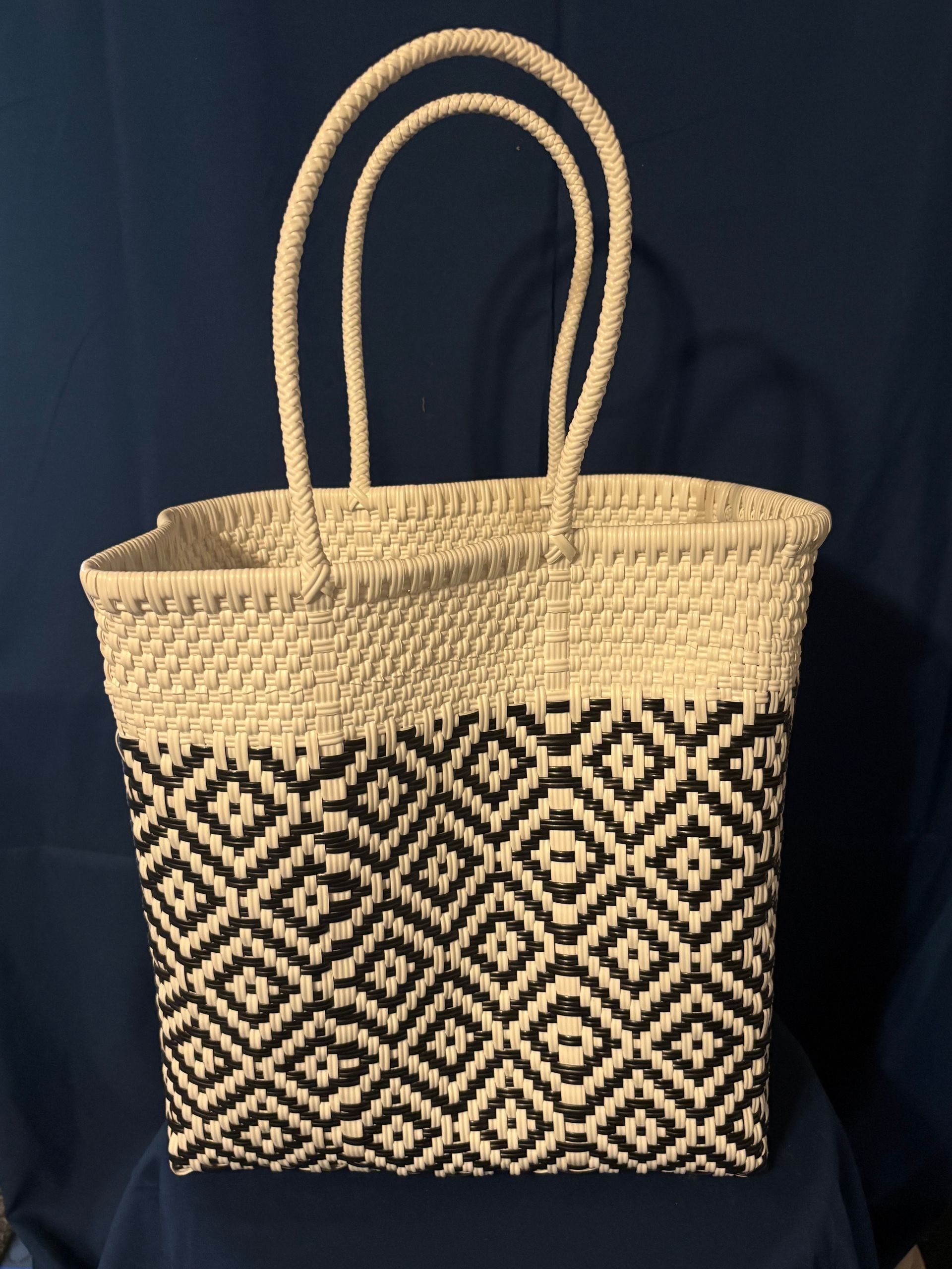 Woven straw tote bag with black-and-cream geometric pattern and double loop handles on a dark background