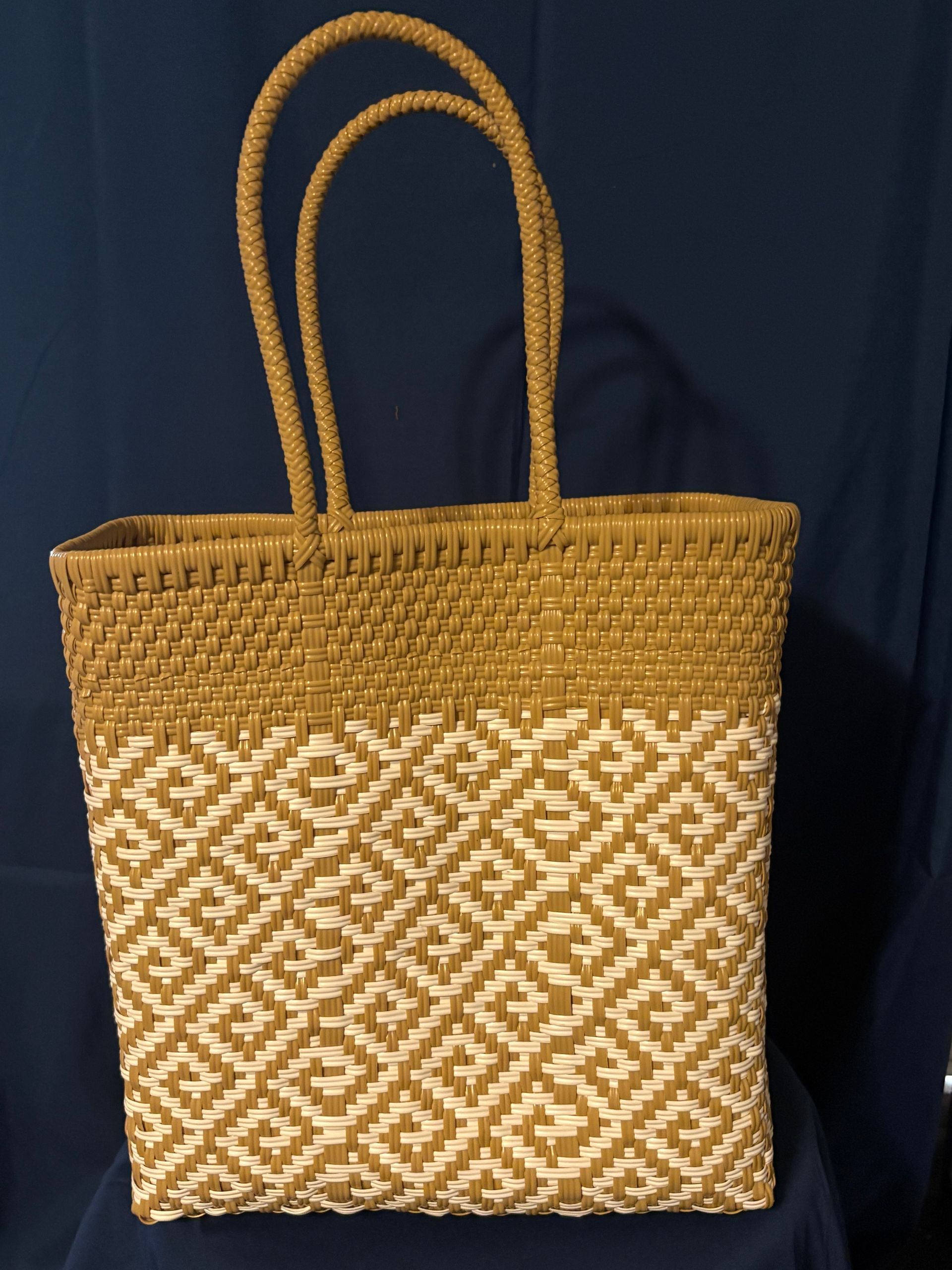 Woven straw tote bag with tan handles and a white geometric pattern on a dark background