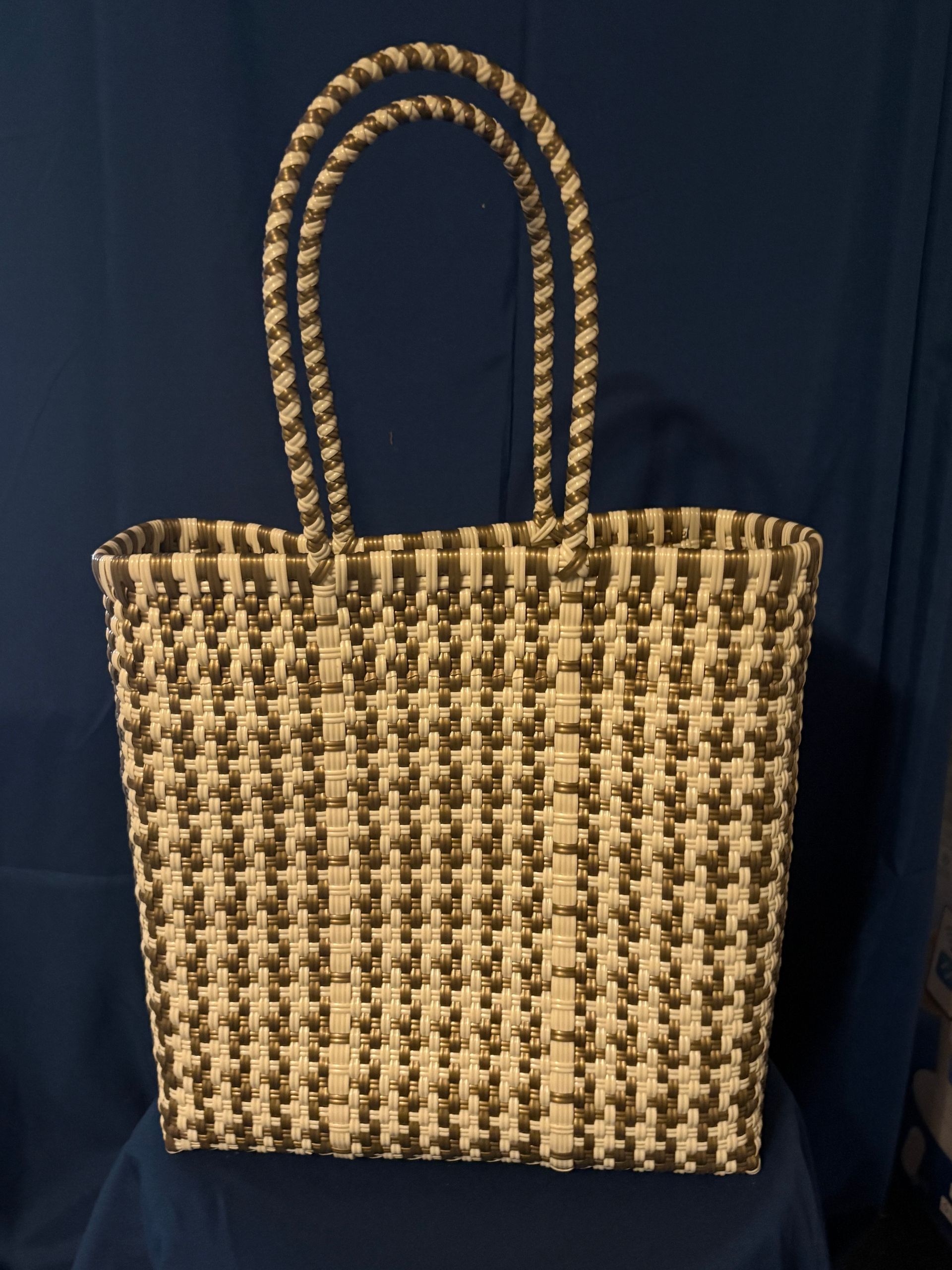 Woven straw tote bag with two handles, beige and dark brown, against a dark blue background
