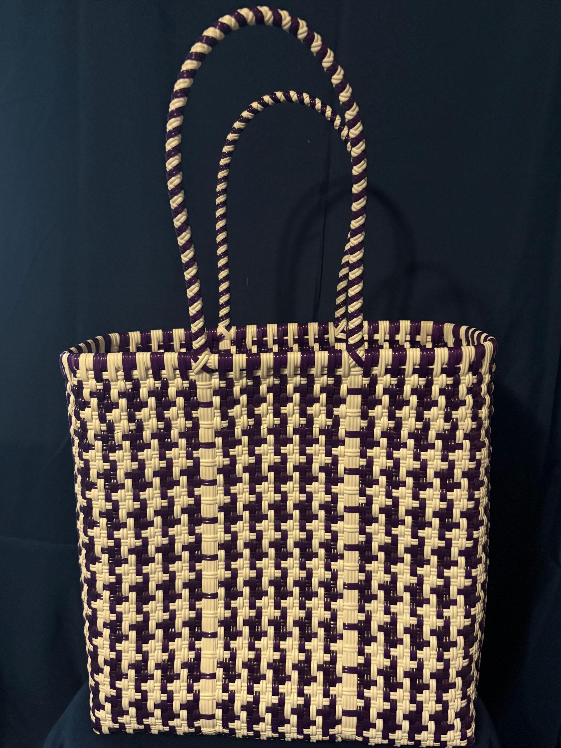 Black-and-tan woven tote bag with two handles on a dark background