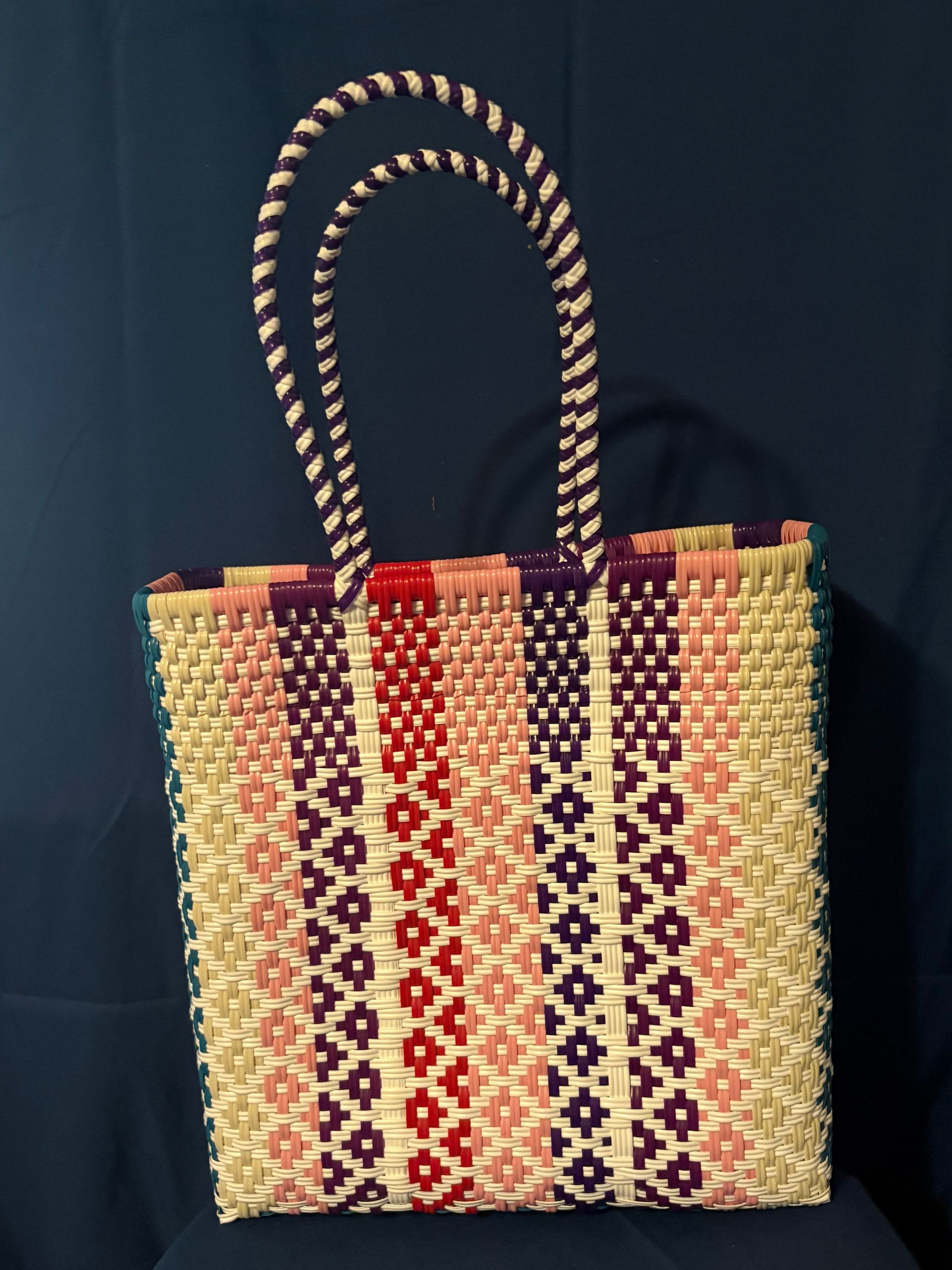 Woven tote bag with colorful geometric patterns and striped handles against a dark background