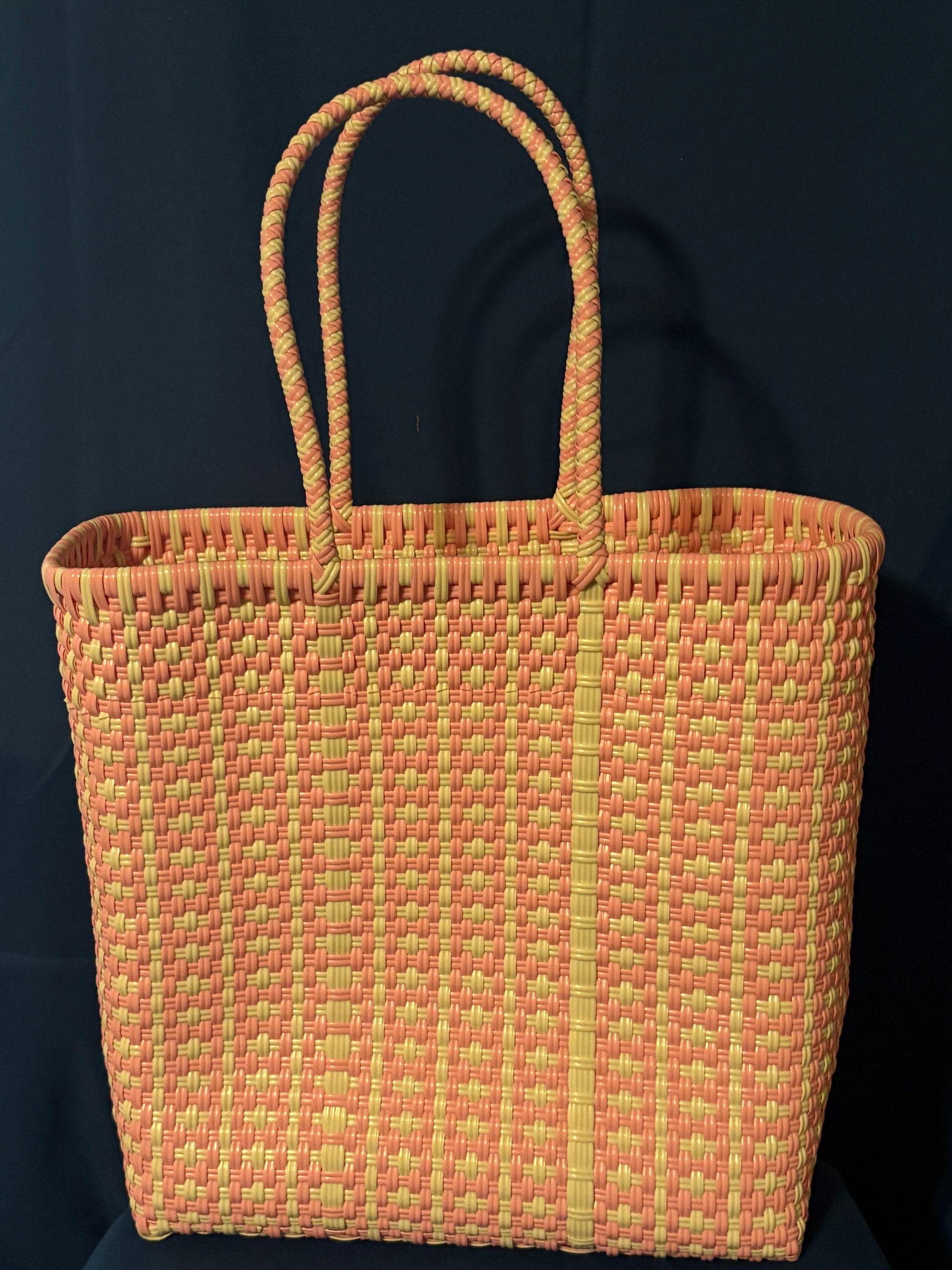 Orange woven tote bag with two loop handles on a dark background