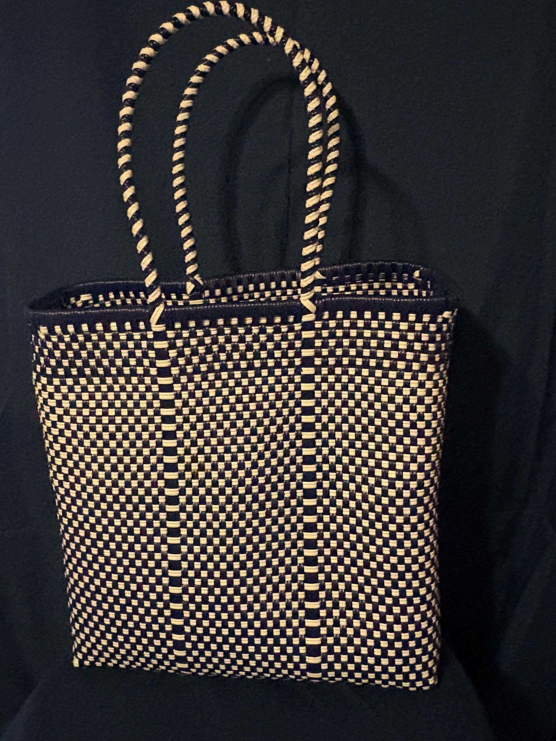 Black woven handbag with tan handles on a dark background