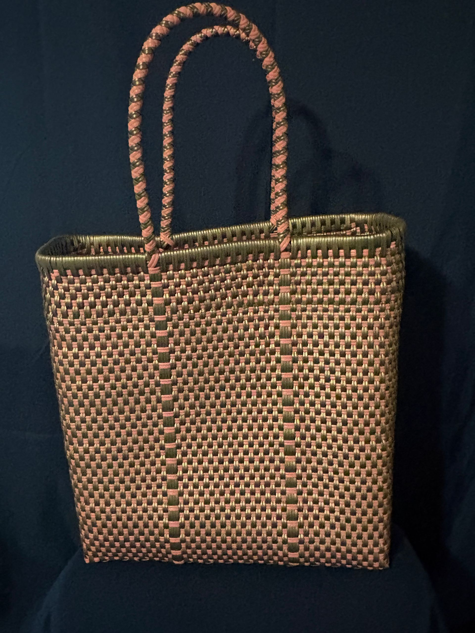Brown woven tote bag with two arched handles on a dark background