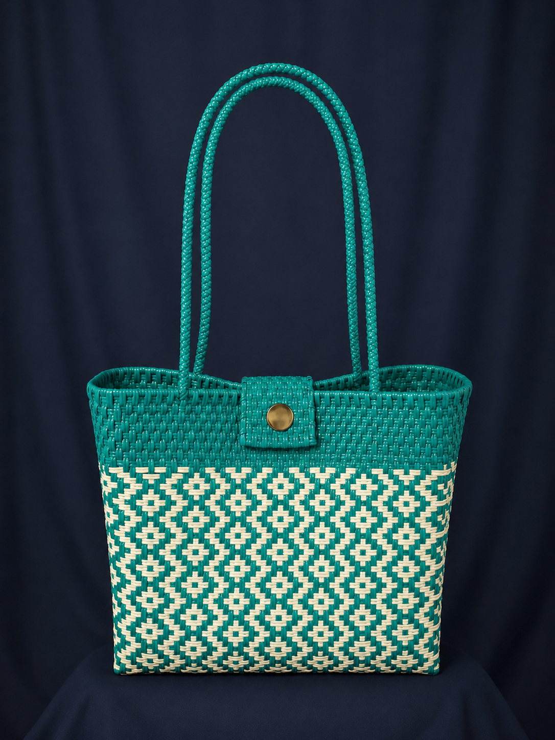 Teal woven tote bag with long handles and patterned lower half on a dark background