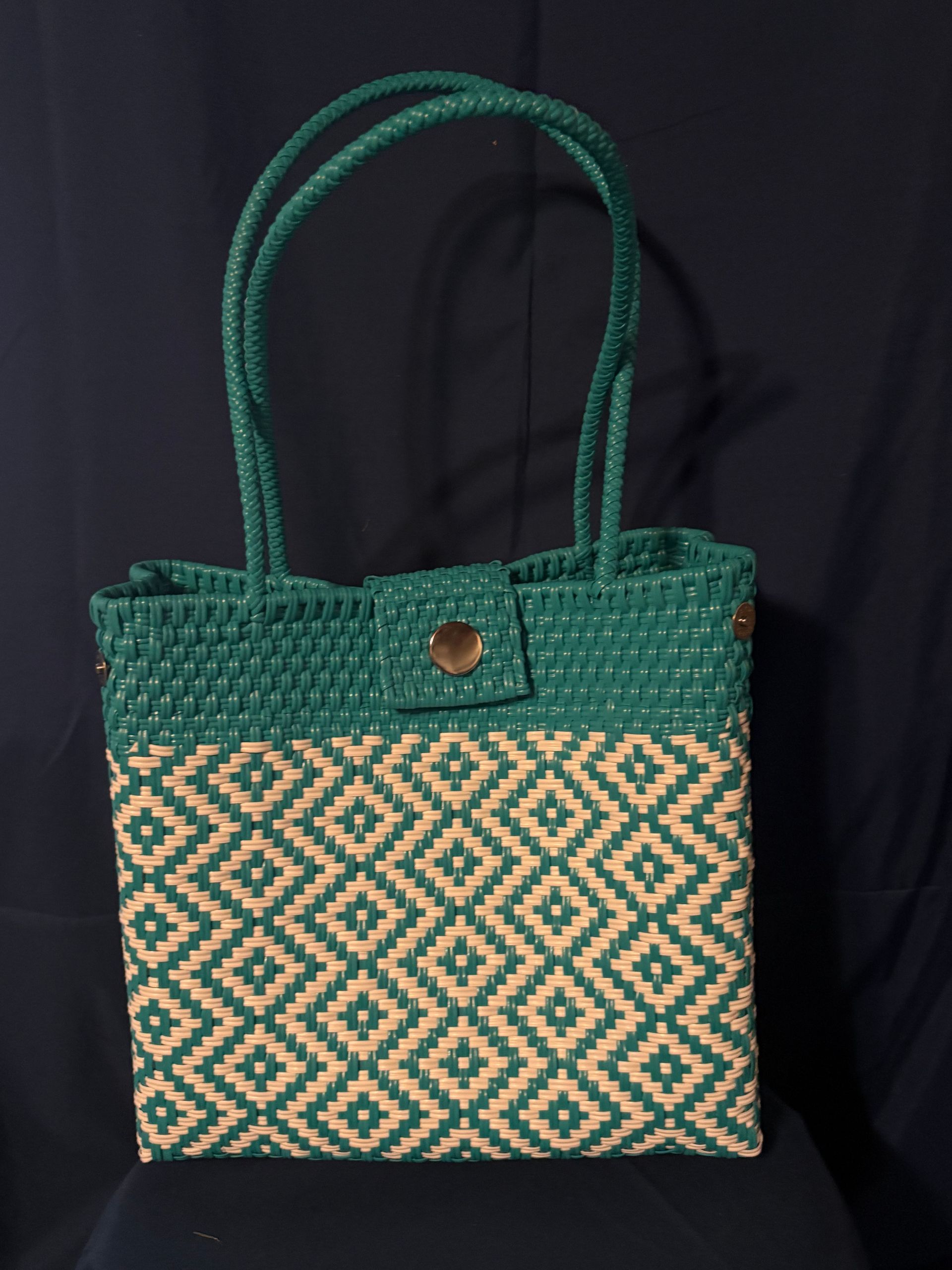 Green woven tote bag with tan geometric pattern and double handles on a dark background
