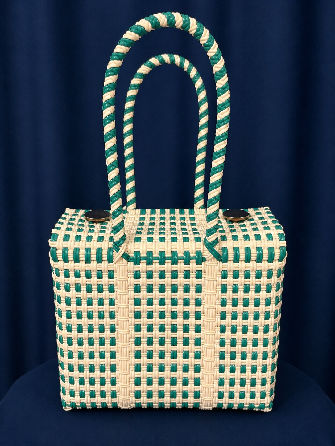 Green-and-cream woven handbag with a tall loop handle against a dark blue background