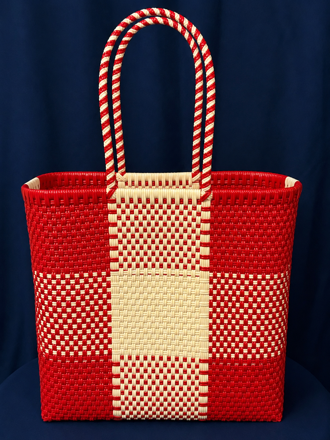 Red woven tote bag with a red-and-white checkered handle and center stripe on a dark blue background