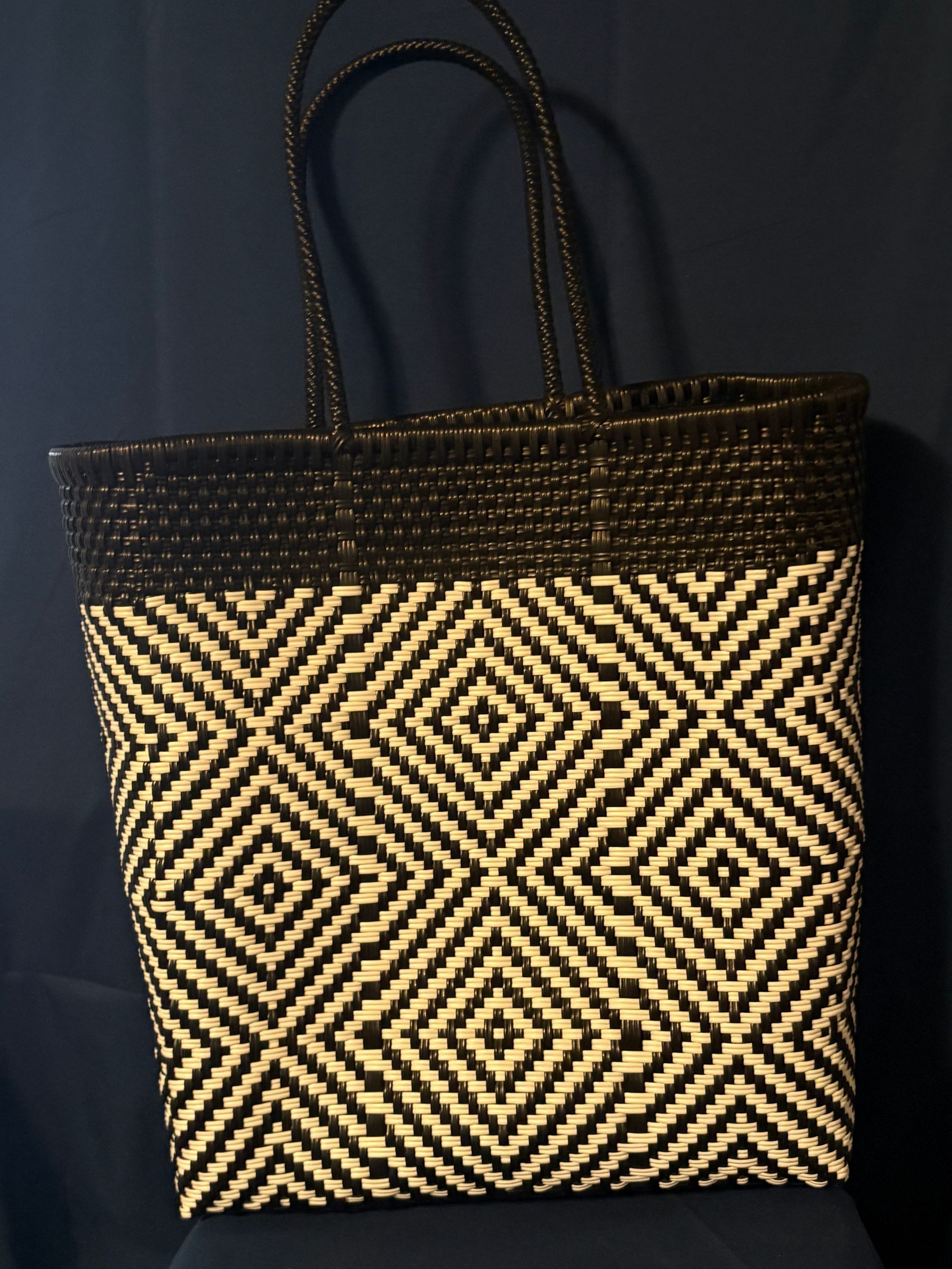 Black-and-tan woven tote bag with geometric diamond pattern and double handles on a dark background