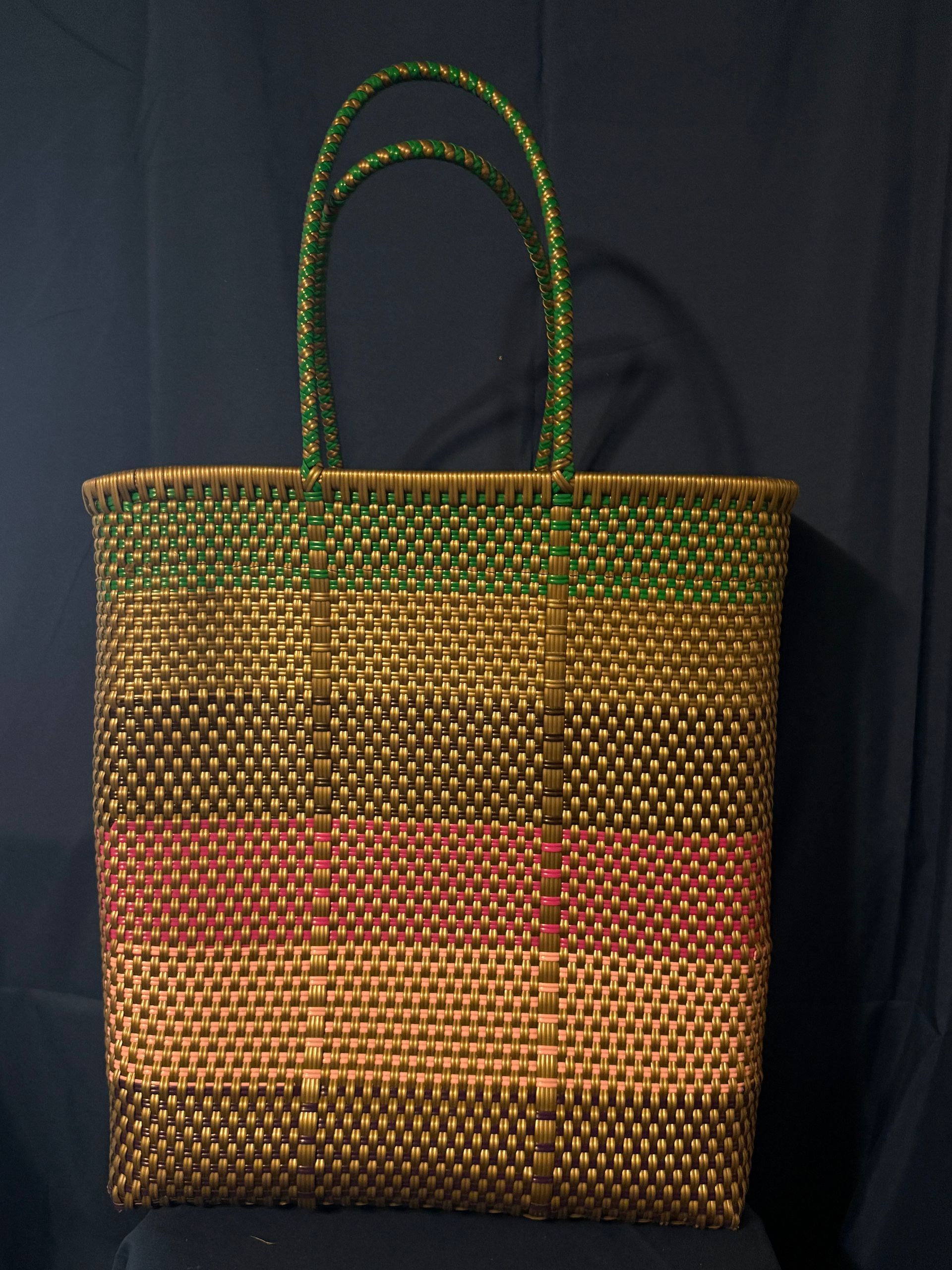 Woven multicolored tote bag with green handles against a dark background