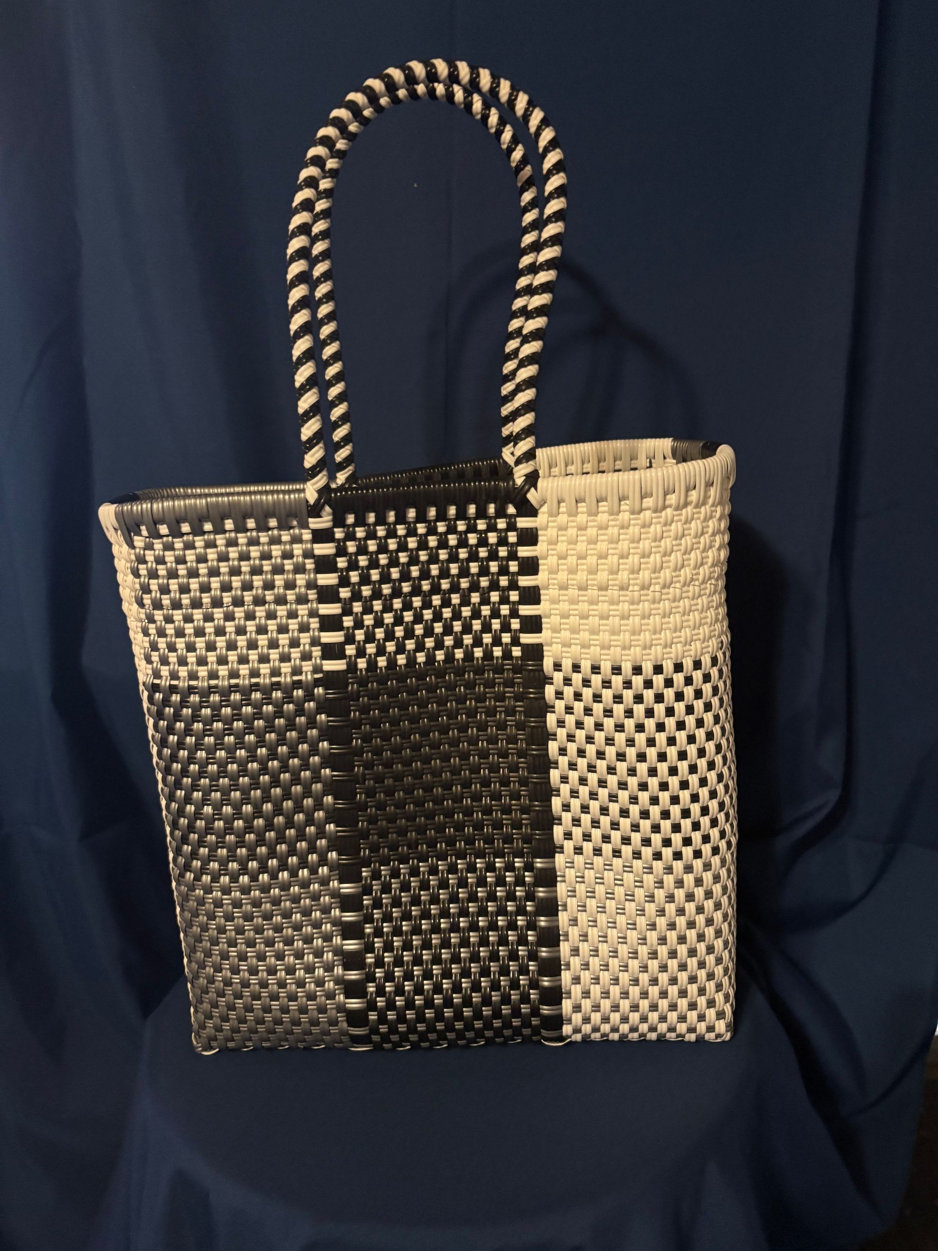 Black-and-white woven tote bag with braided handles on a dark blue fabric background