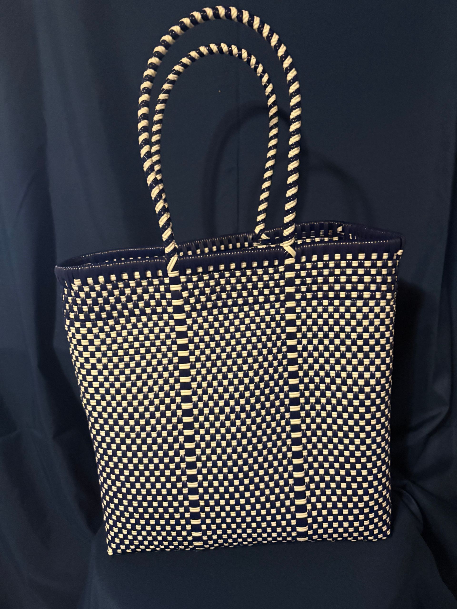 Black tote bag with gold polka dots and braided handles against a dark background