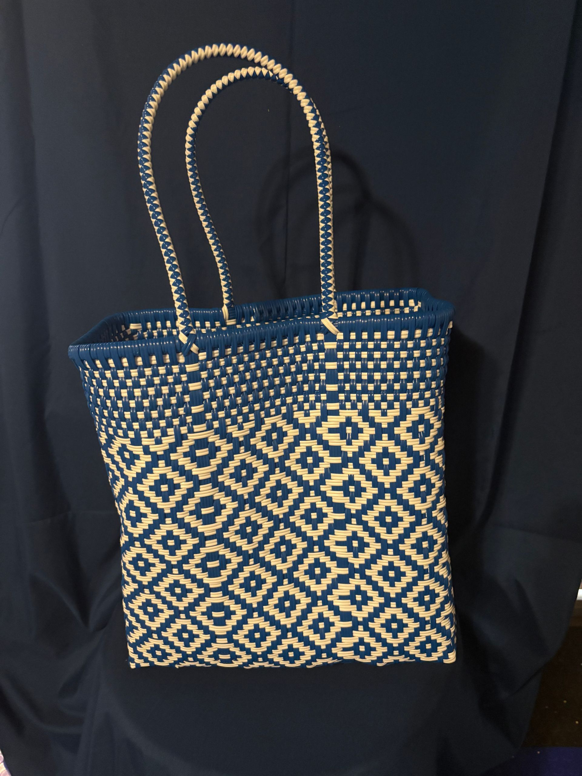 Blue-and-cream patterned tote bag with long beaded handles against a dark background