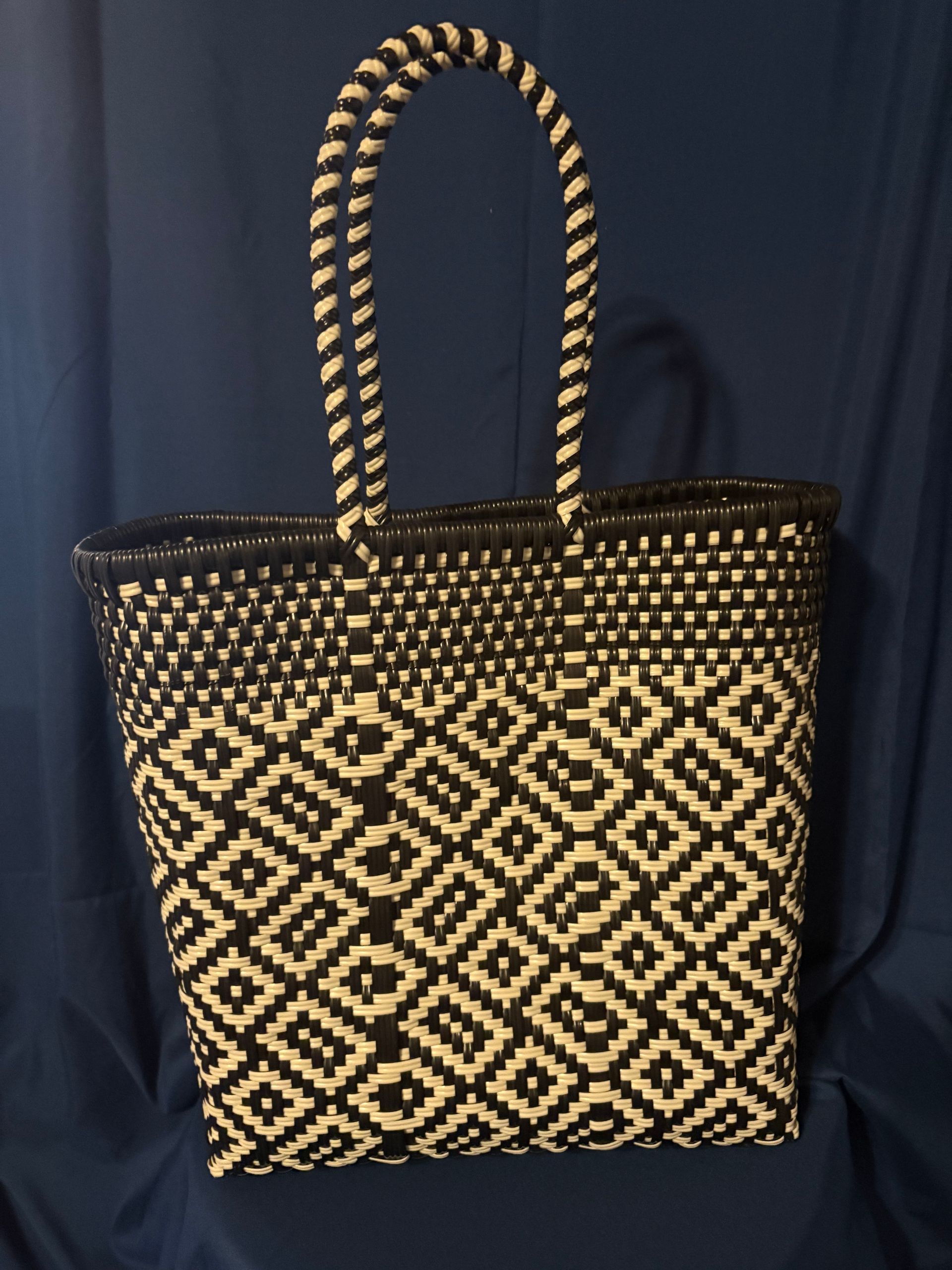 Black and tan patterned woven tote bag with braided handles on a dark background