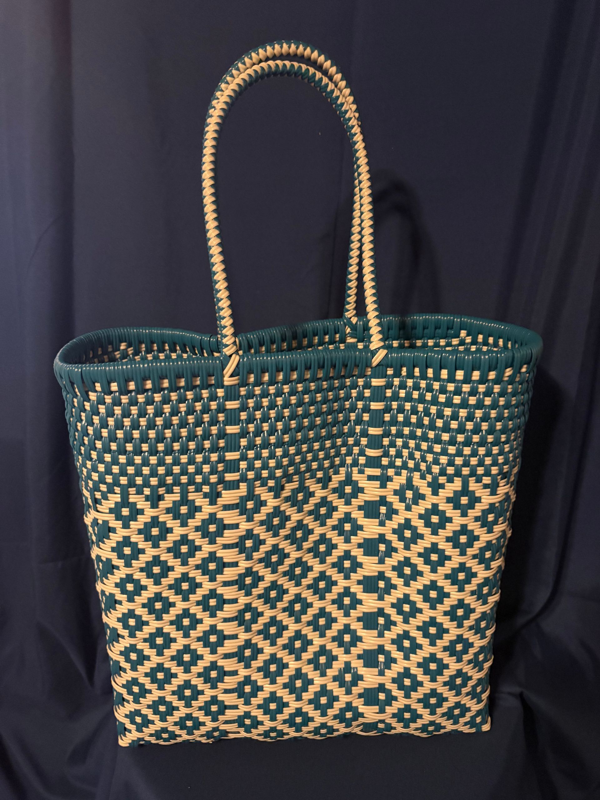 Teal woven tote bag with tan handles and geometric pattern against a dark backdrop