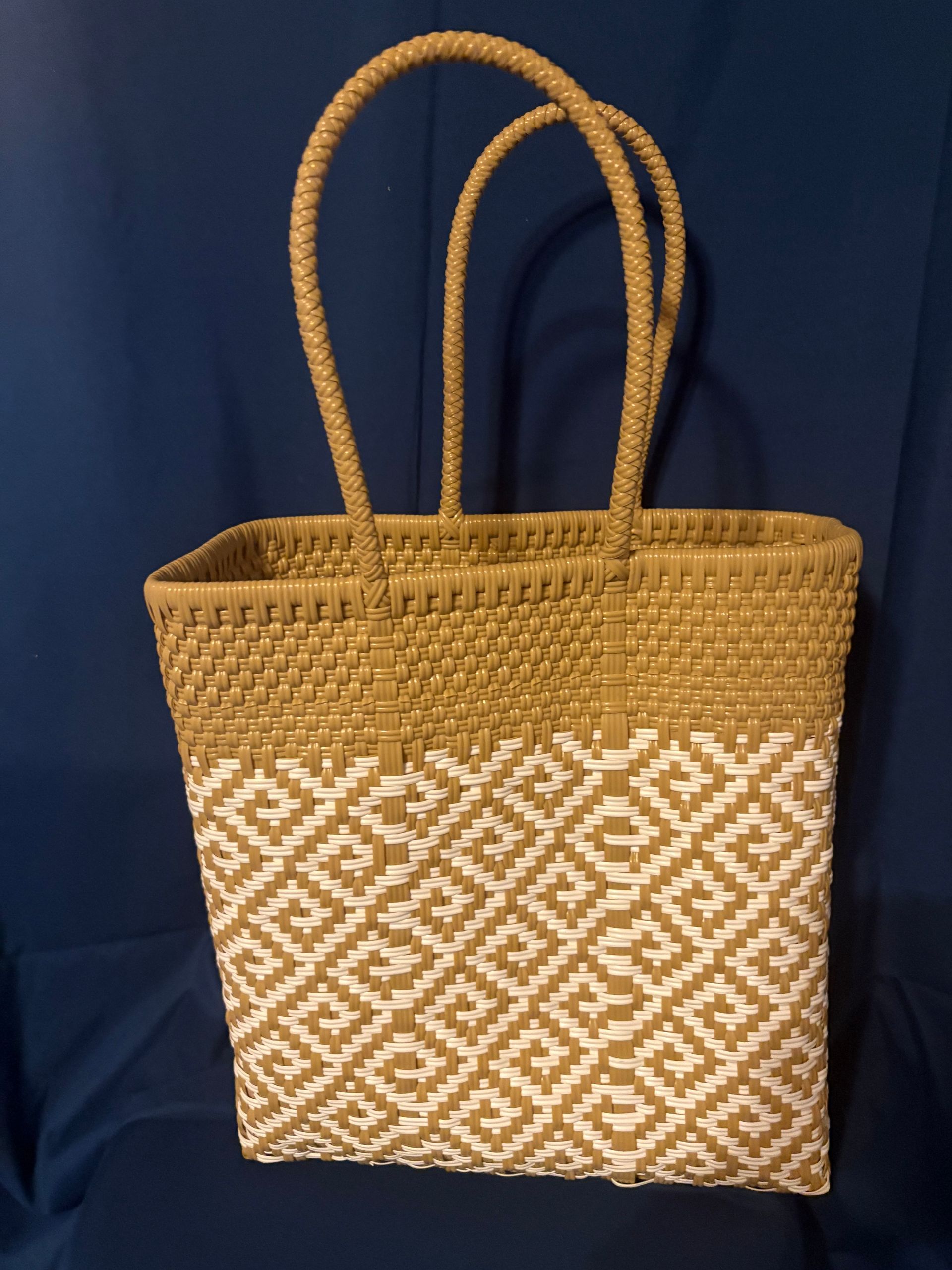 Woven tan tote bag with braided handles and white geometric pattern on a blue background