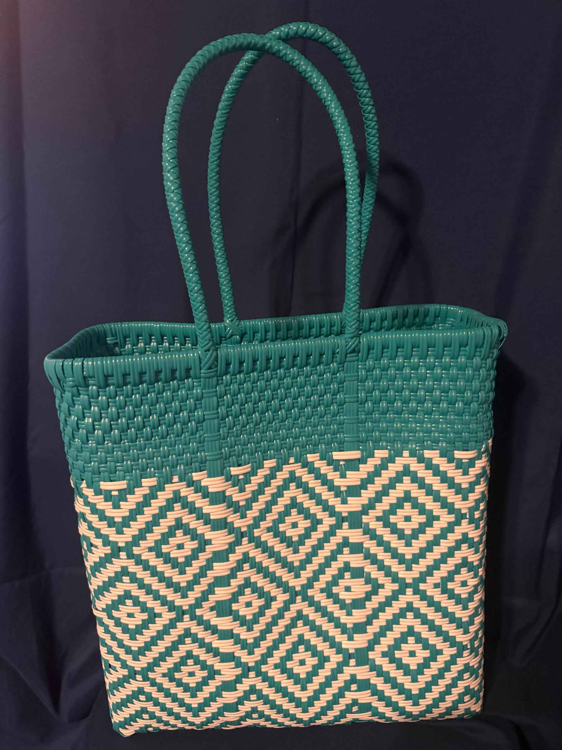 Green woven tote bag with tan geometric pattern and twin handles against a dark background