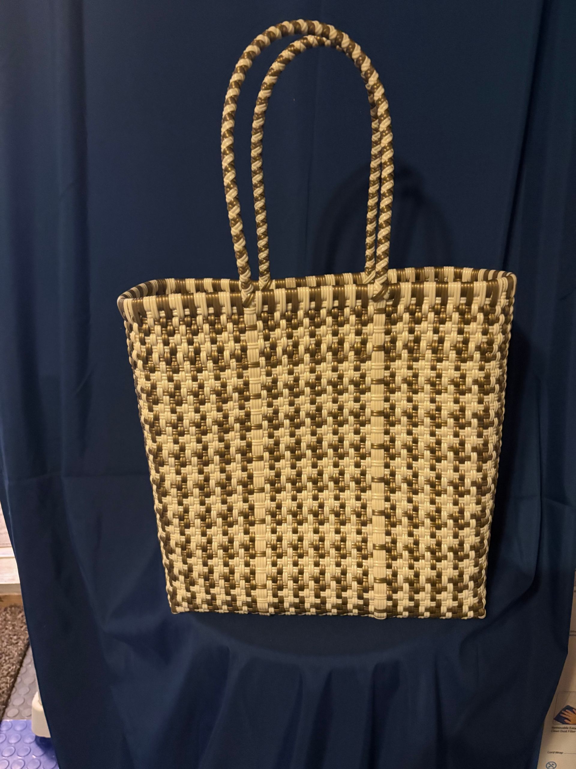 Woven beige-and-black tote bag with braided handles on a dark blue backdrop
