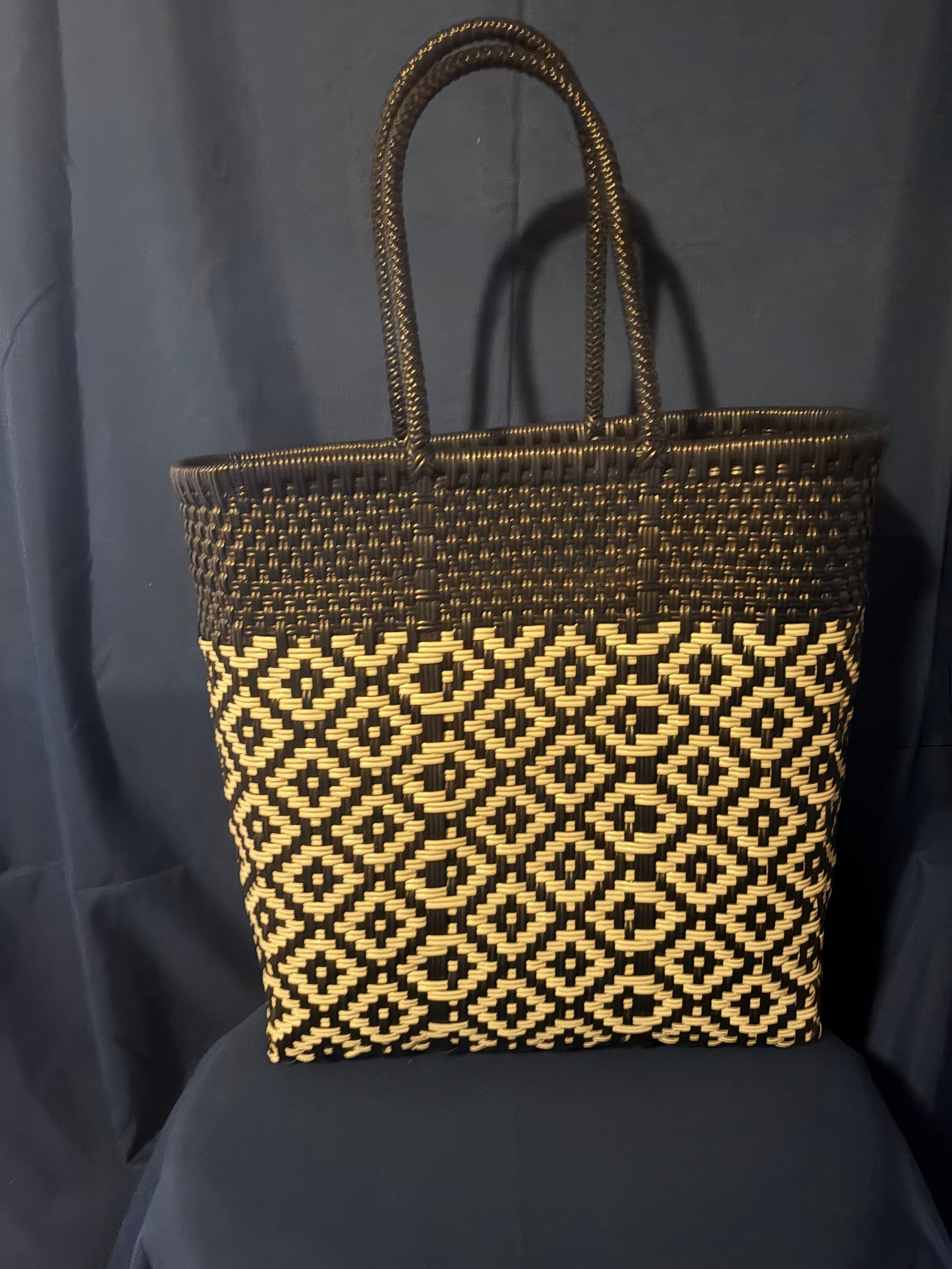 Black and tan woven tote bag with patterned front, standing against a dark background