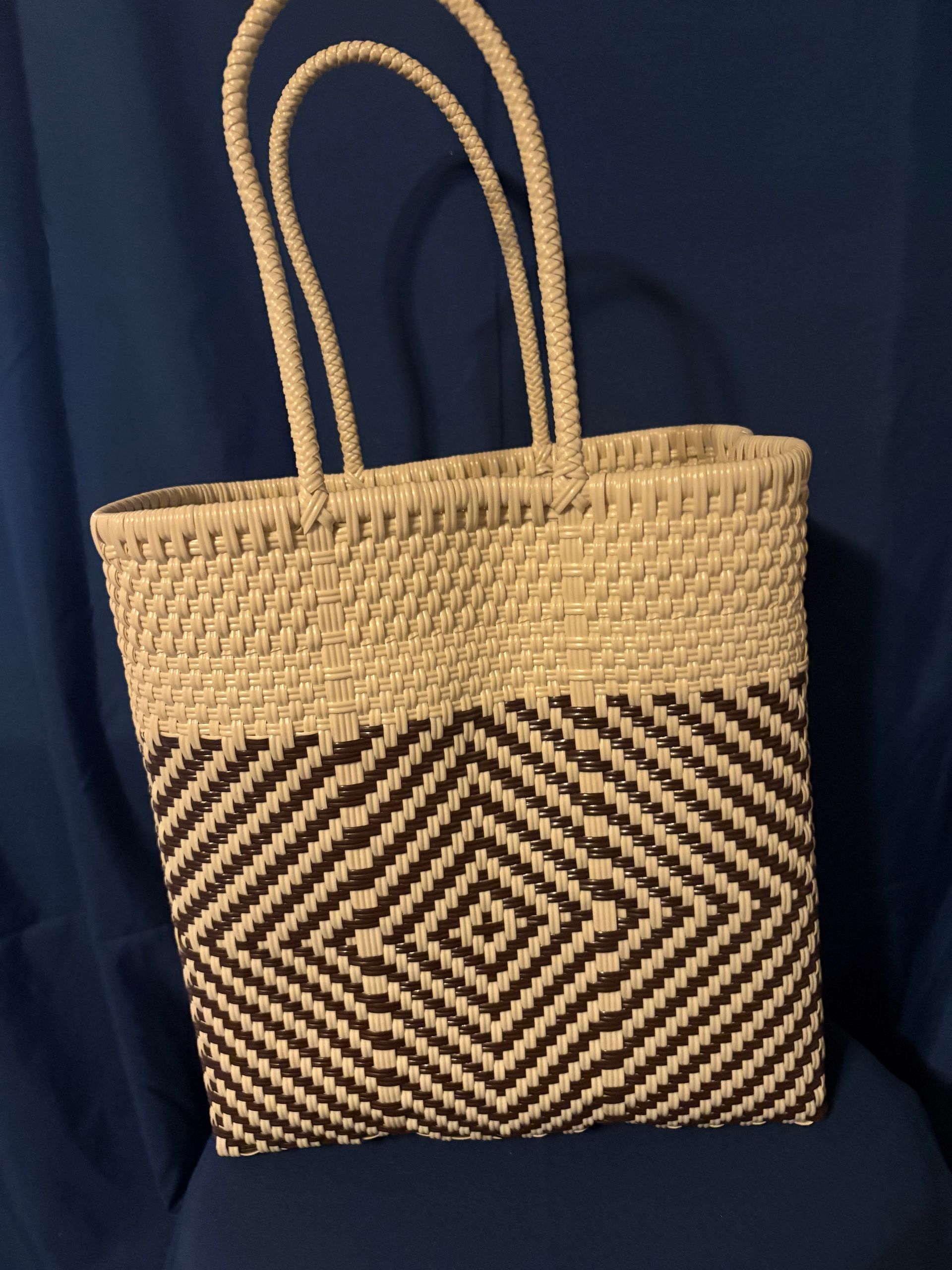 Woven straw tote bag with tan handles and black-and-tan geometric pattern on a dark blue background